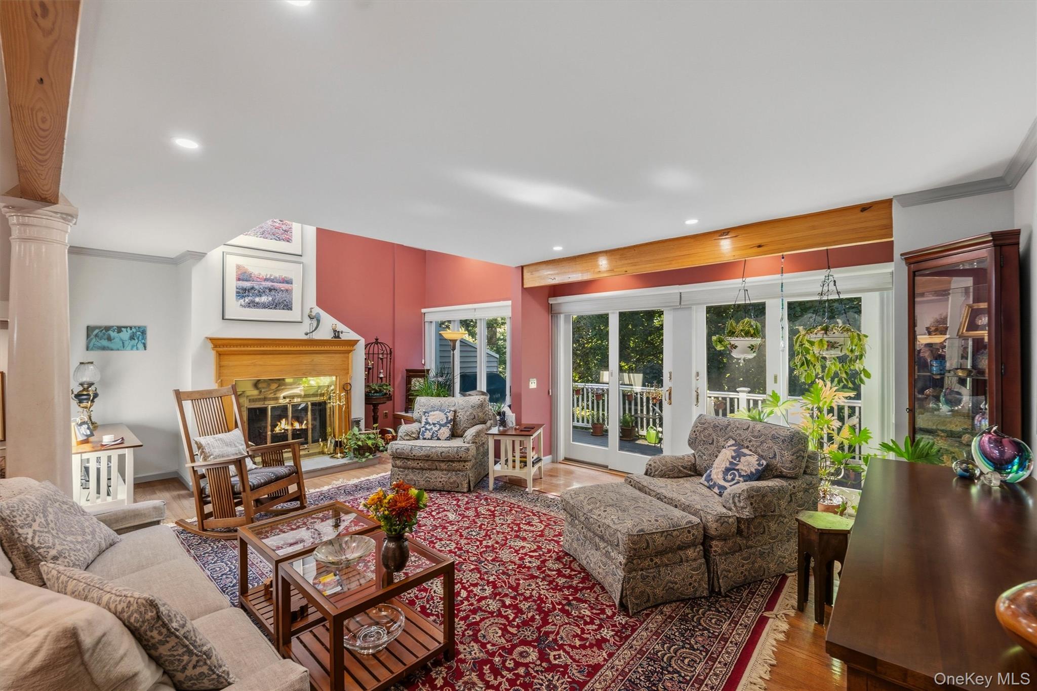 Living room with a wood-trimmed fireplace, patterned seating, red rug, and glass doors to a deck.