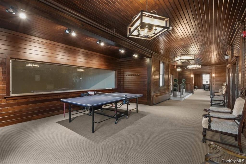 Recreation room with a ping-pong table, dark wood paneling, carpet, and chairs.