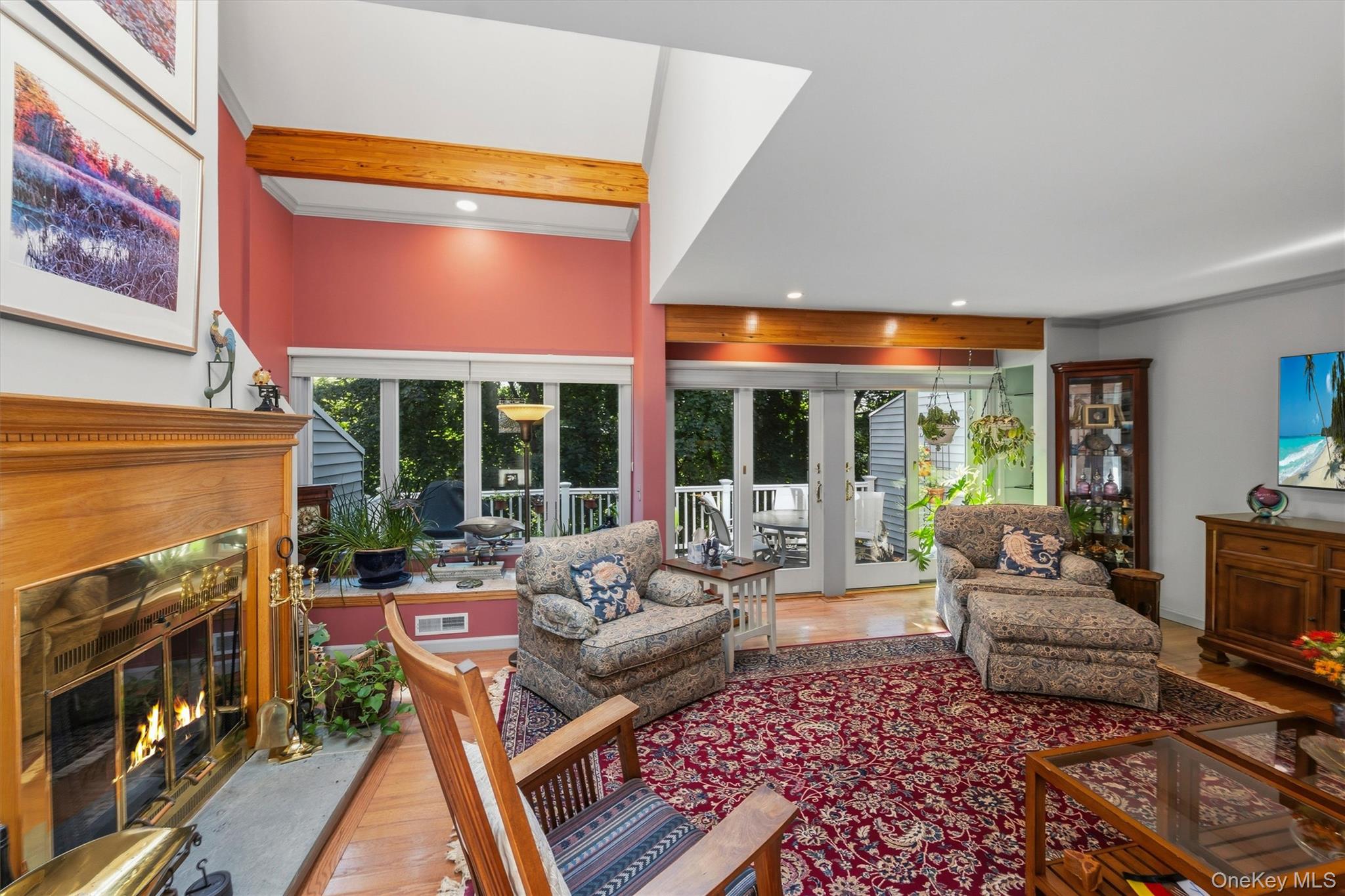Living room with vaulted ceiling, wood beams, fireplace, patterned seating, and glass doors to a deck.
