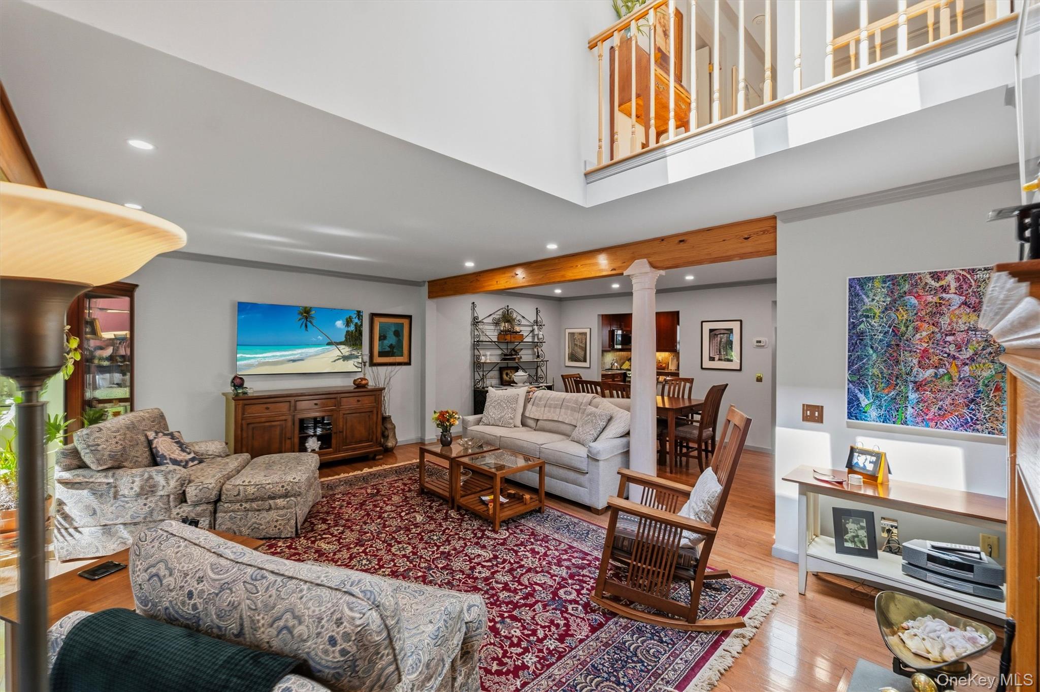 Living room with an open upper-level railing, exposed wood beam, and hardwood floors.