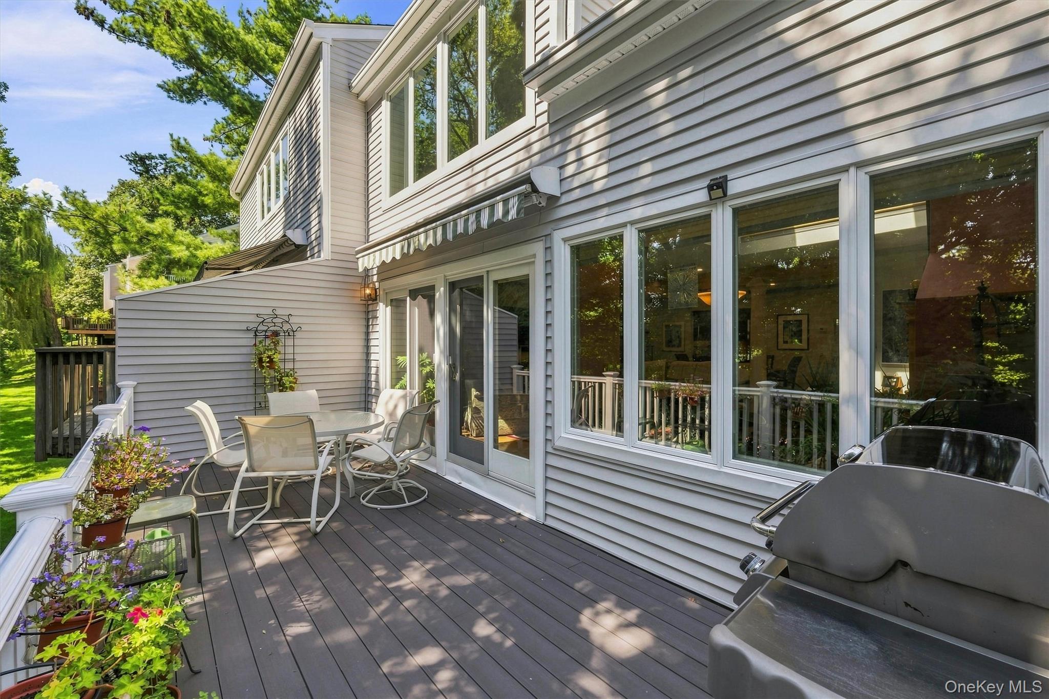 Rear deck with patio dining set, potted flowers, sliding glass doors, and a large grill.