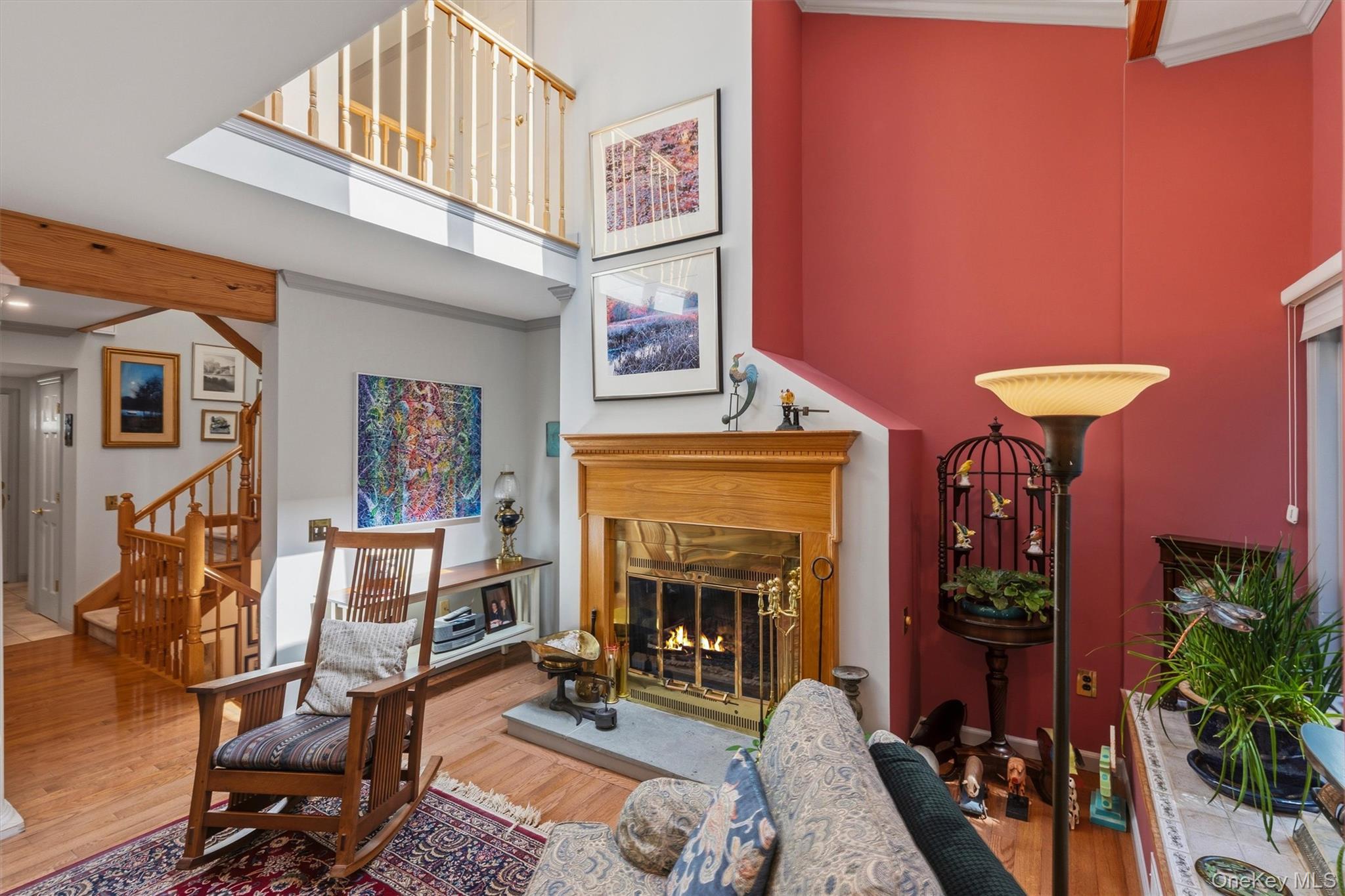 Living room with a wood fireplace, vaulted ceiling, red accent wall, and hardwood floors.