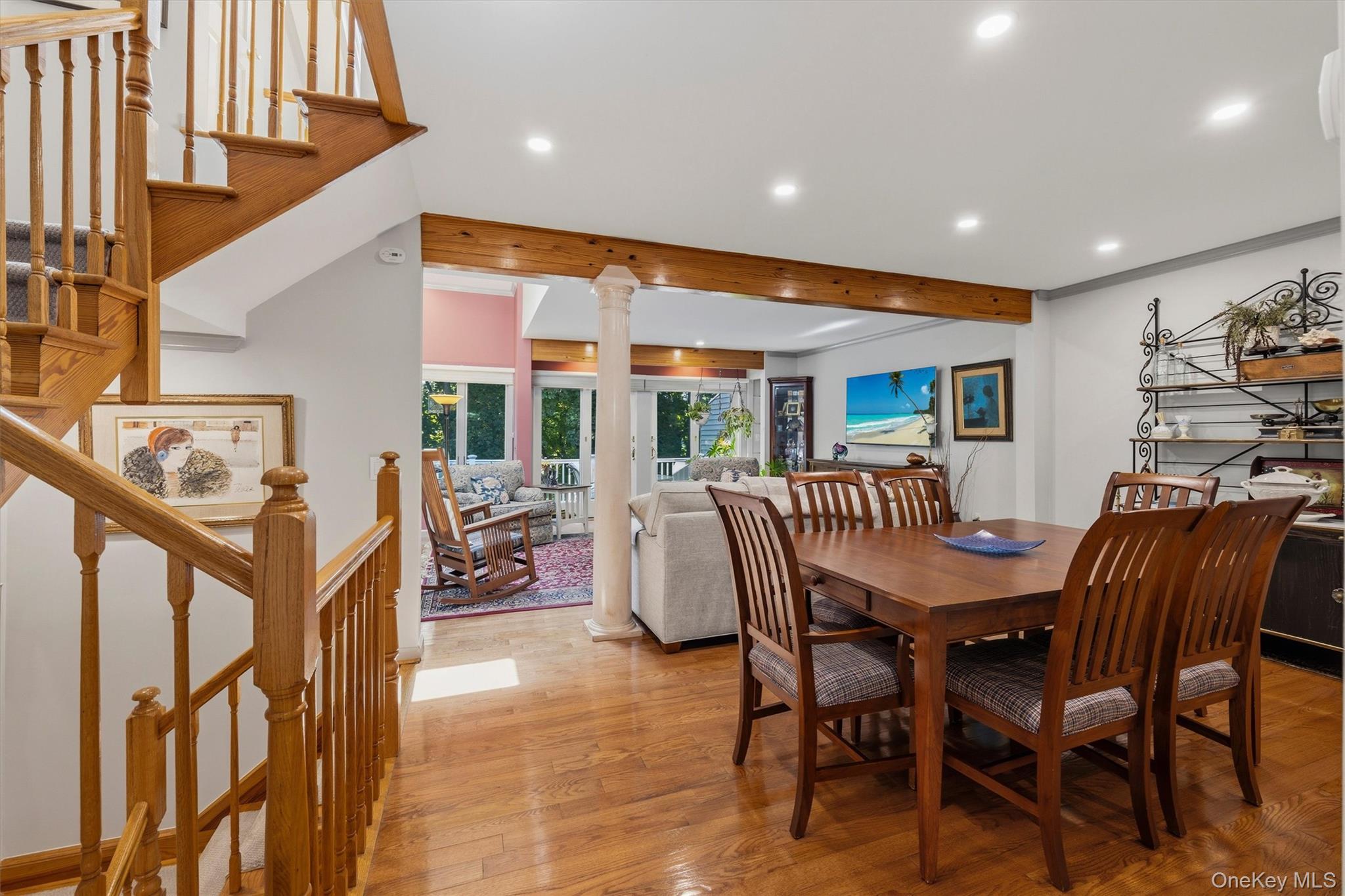 Dining area with hardwood floors and wooden staircase opening to a living area by glass doors.