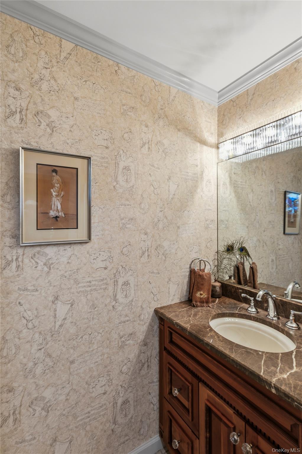 Bathroom vanity with a brown marble countertop, dark wood cabinet, large mirror, and ornate beige wallpaper.