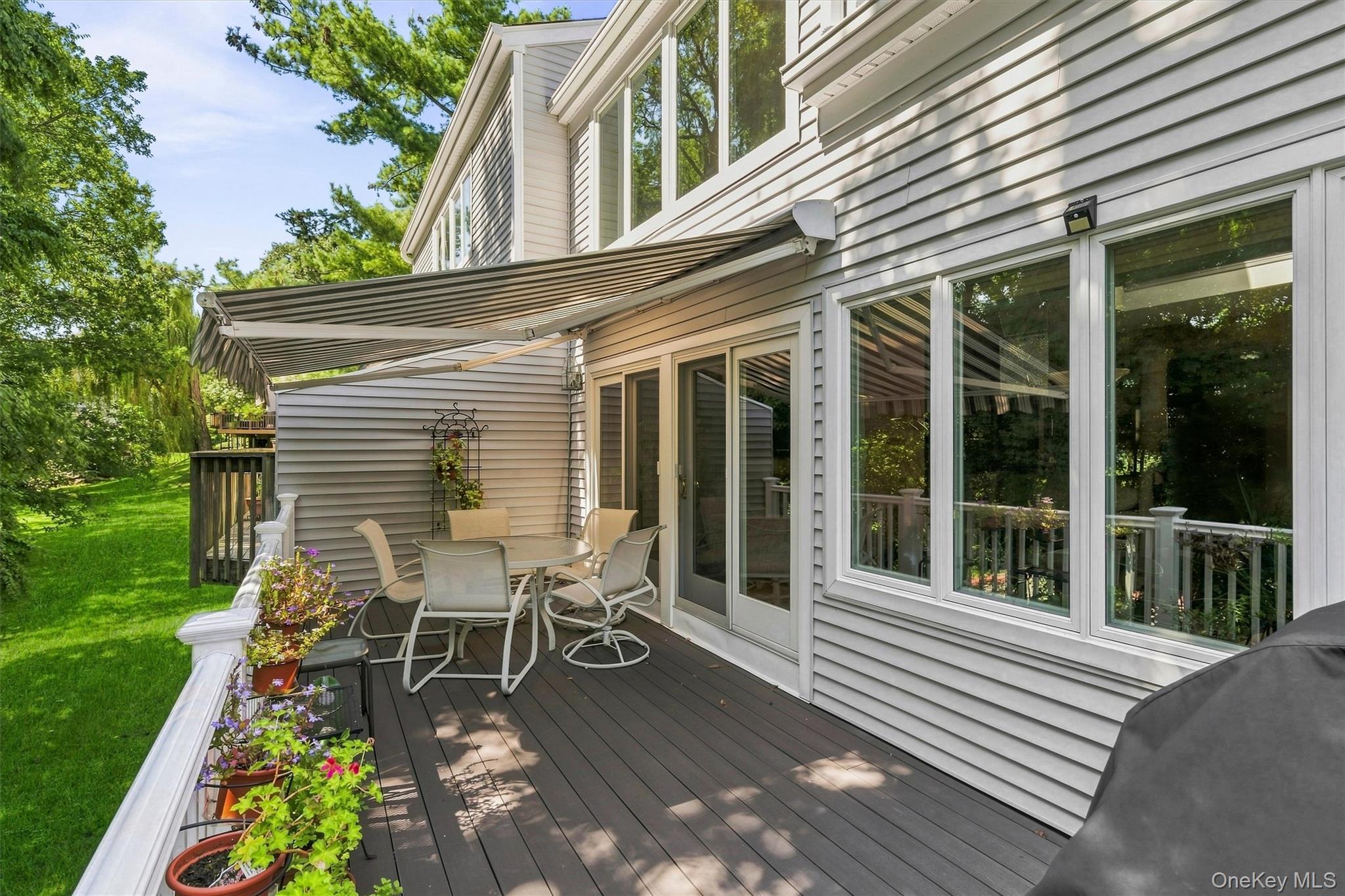 Backyard deck with retractable awning, outdoor dining set, potted flowers, and lawn.