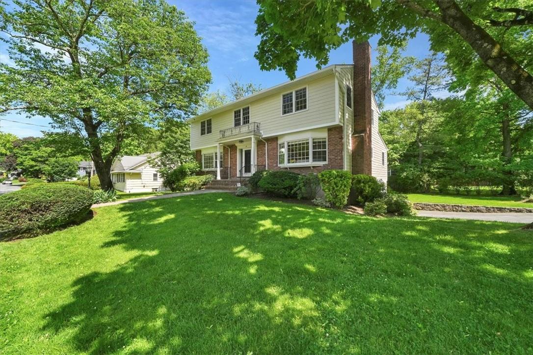 Two-story house with brick accents and a small balcony, framed by mature trees and a broad lawn.