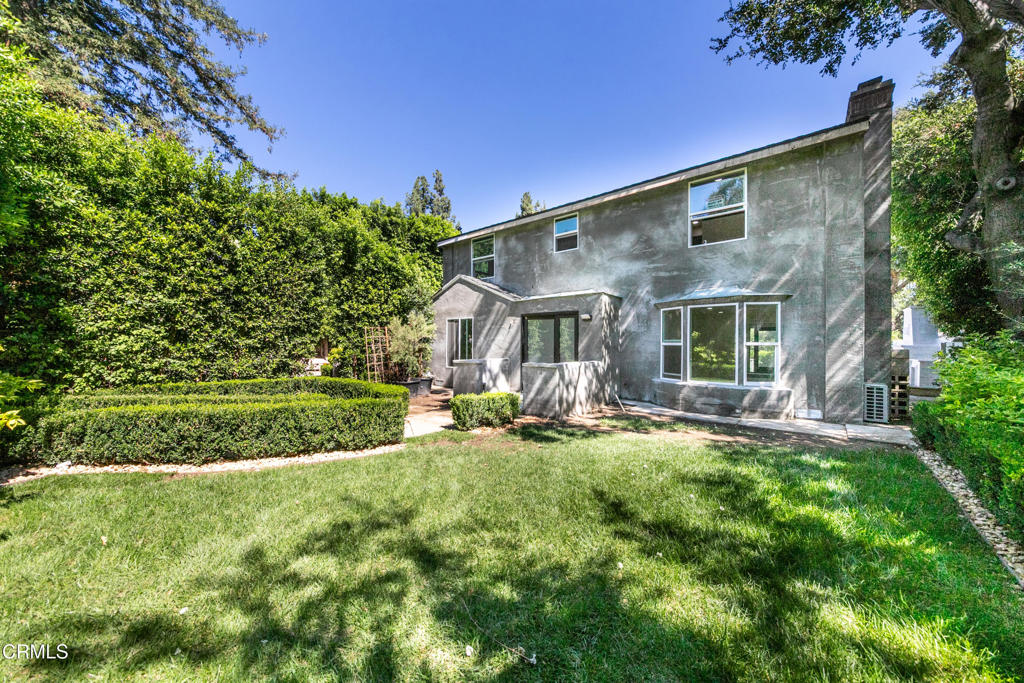 Rear of a two-story gray house with a broad lawn and clipped hedges.