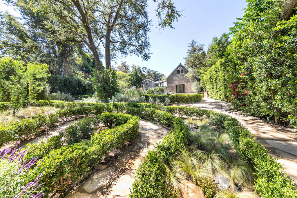 Home beyond a formal landscaped garden with winding stone paths and clipped hedges.