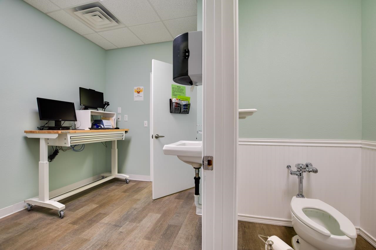 Interior room with a toilet, wall-mounted sink, and wheeled computer workstation.