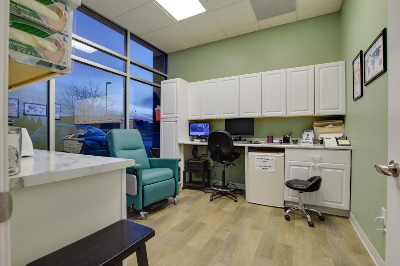 Medical office with white cabinets, computer workstations, and a teal chair beside large windows.