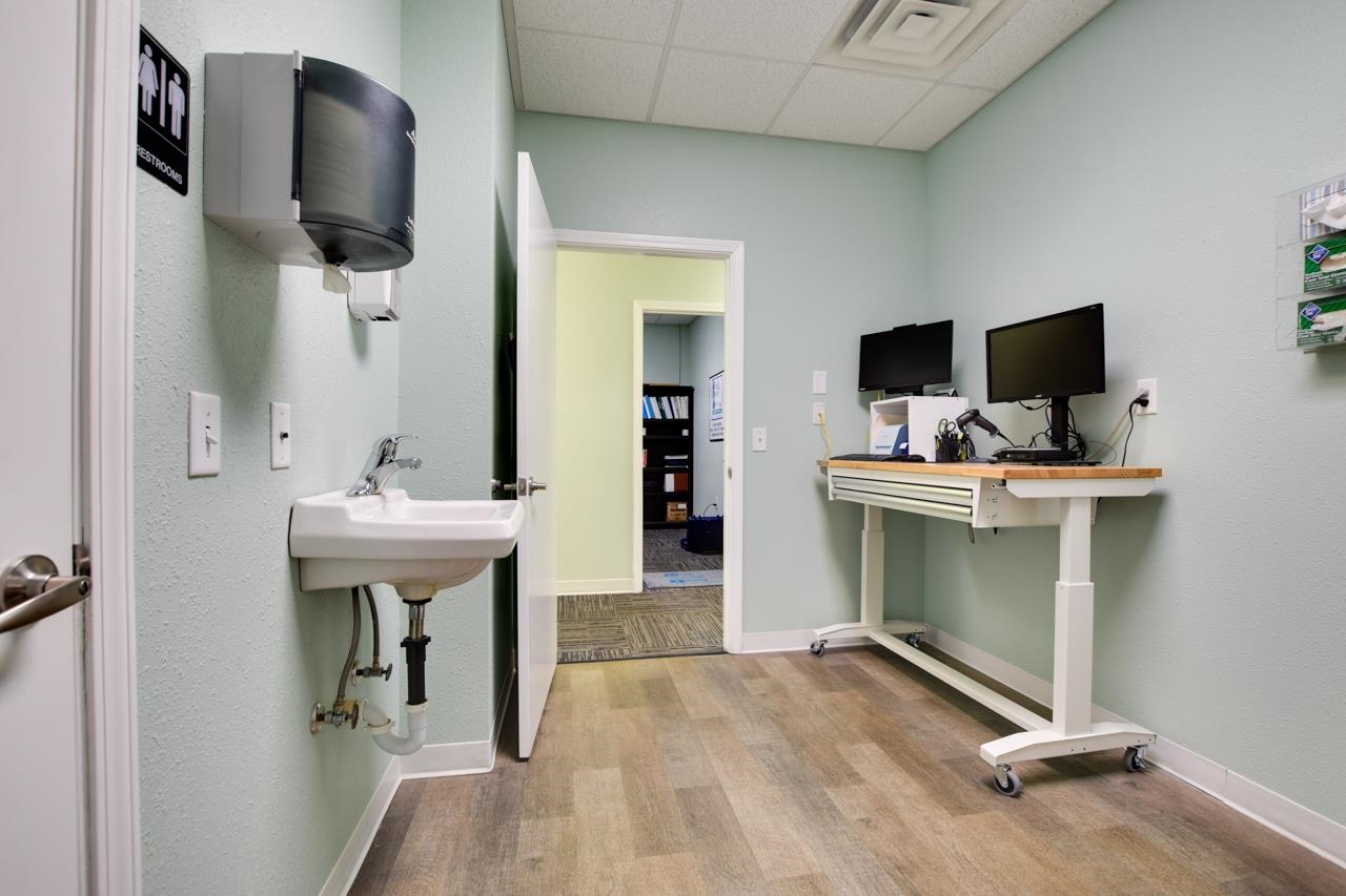 Office room with a wall-mounted sink and wheeled standing desk with two monitors.