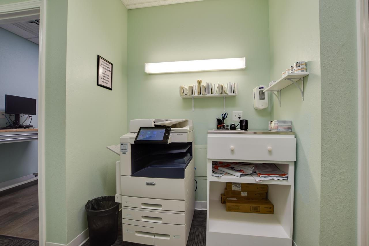 Office workroom with a large copier, white storage cabinet, and shelves of supplies.