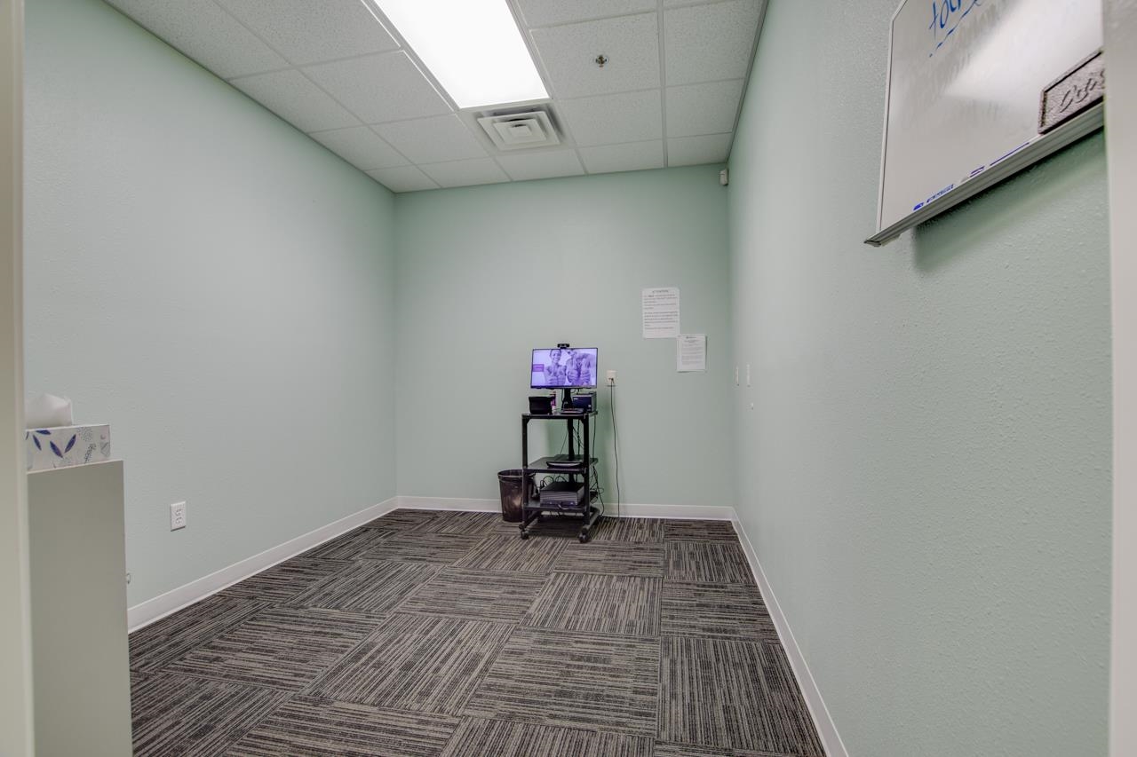 Mostly empty room with pale green walls, patterned carpet tiles, and a wheeled equipment cart.