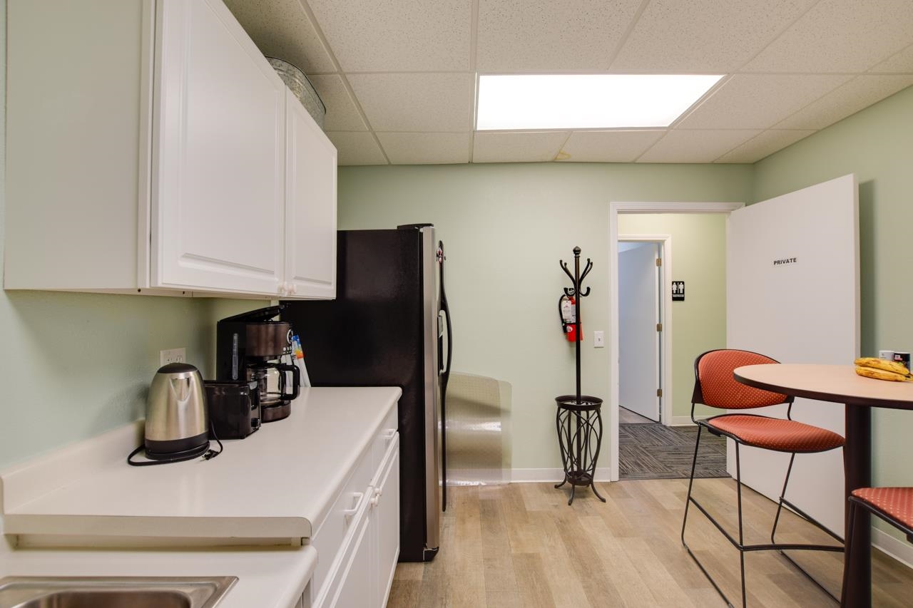 Office break room with white cabinets, a coffee station, and a round table with orange chairs.