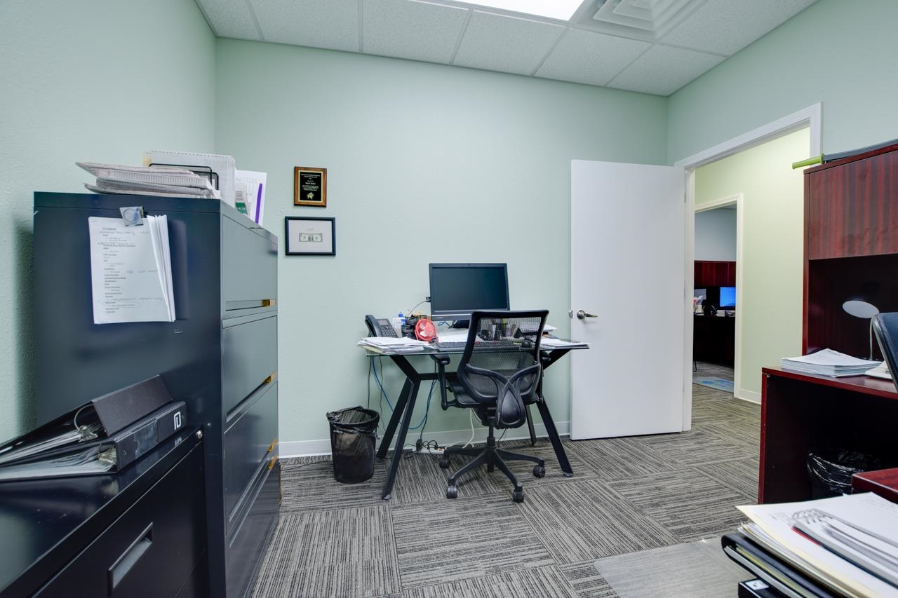Office with a desk and mesh chair, filing cabinets, and an open door to another workspace.