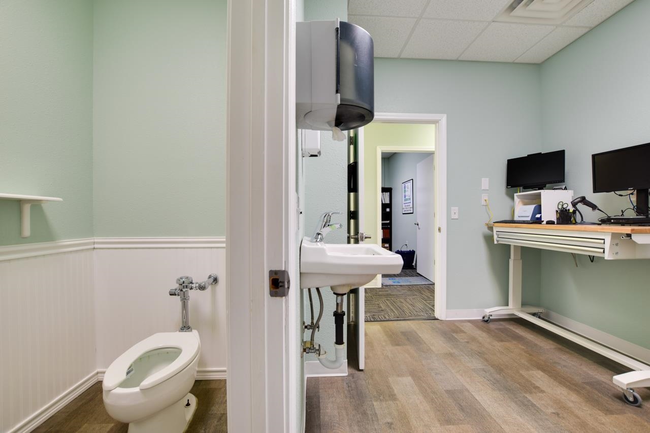 Office workstation beside an open restroom doorway, with a toilet and sink visible.