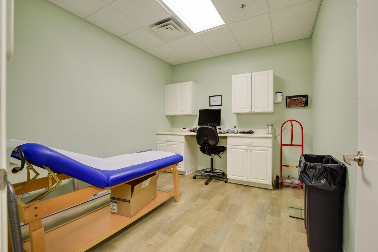 Treatment room with a blue padded table, white cabinets, and a computer workstation.
