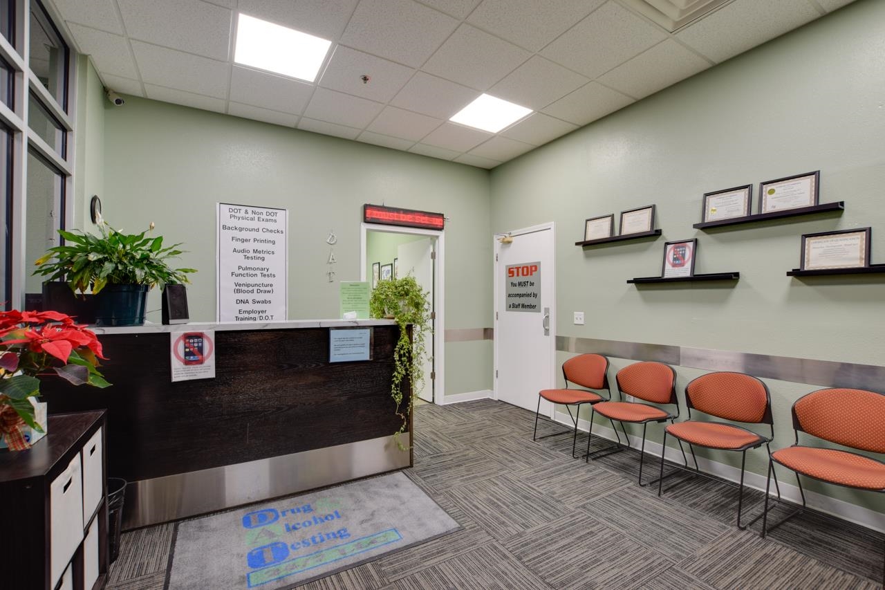 Medical testing office reception with a dark wood counter and orange waiting chairs.