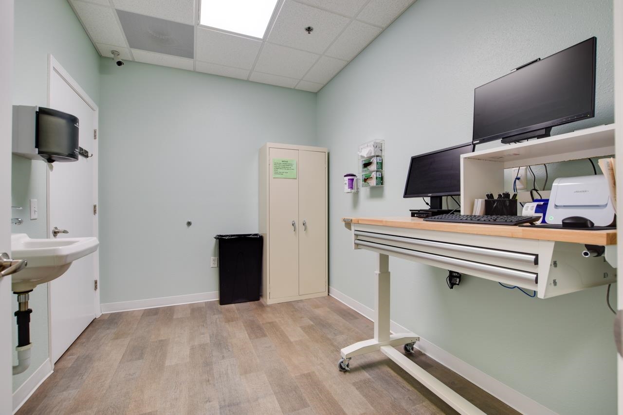 Medical exam room with a sink and wheeled computer workstation.