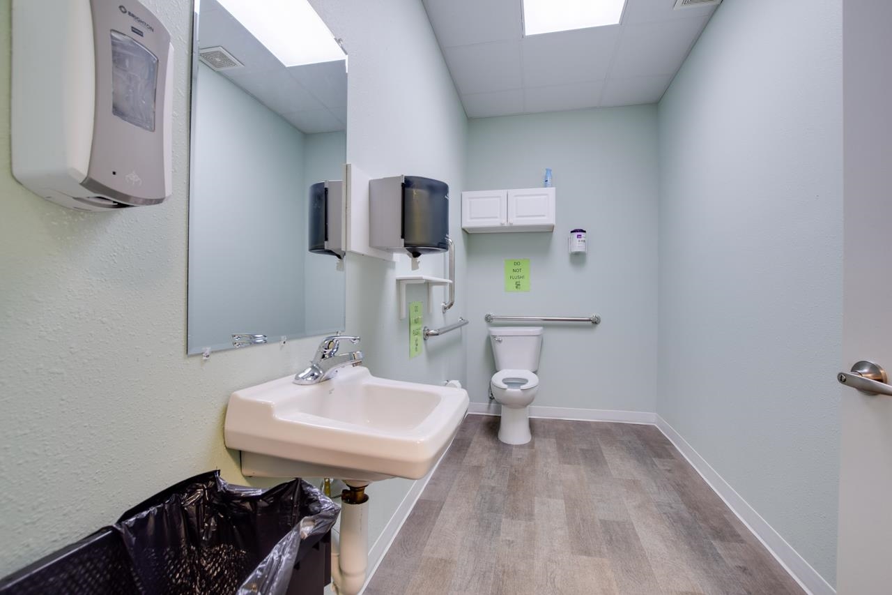 Restroom with a wall-mounted sink, toilet, grab bars, and mirror.