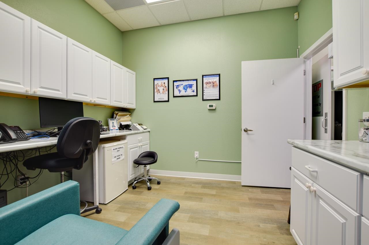 Medical exam room with white cabinetry, a desk, and a teal upholstered exam chair.