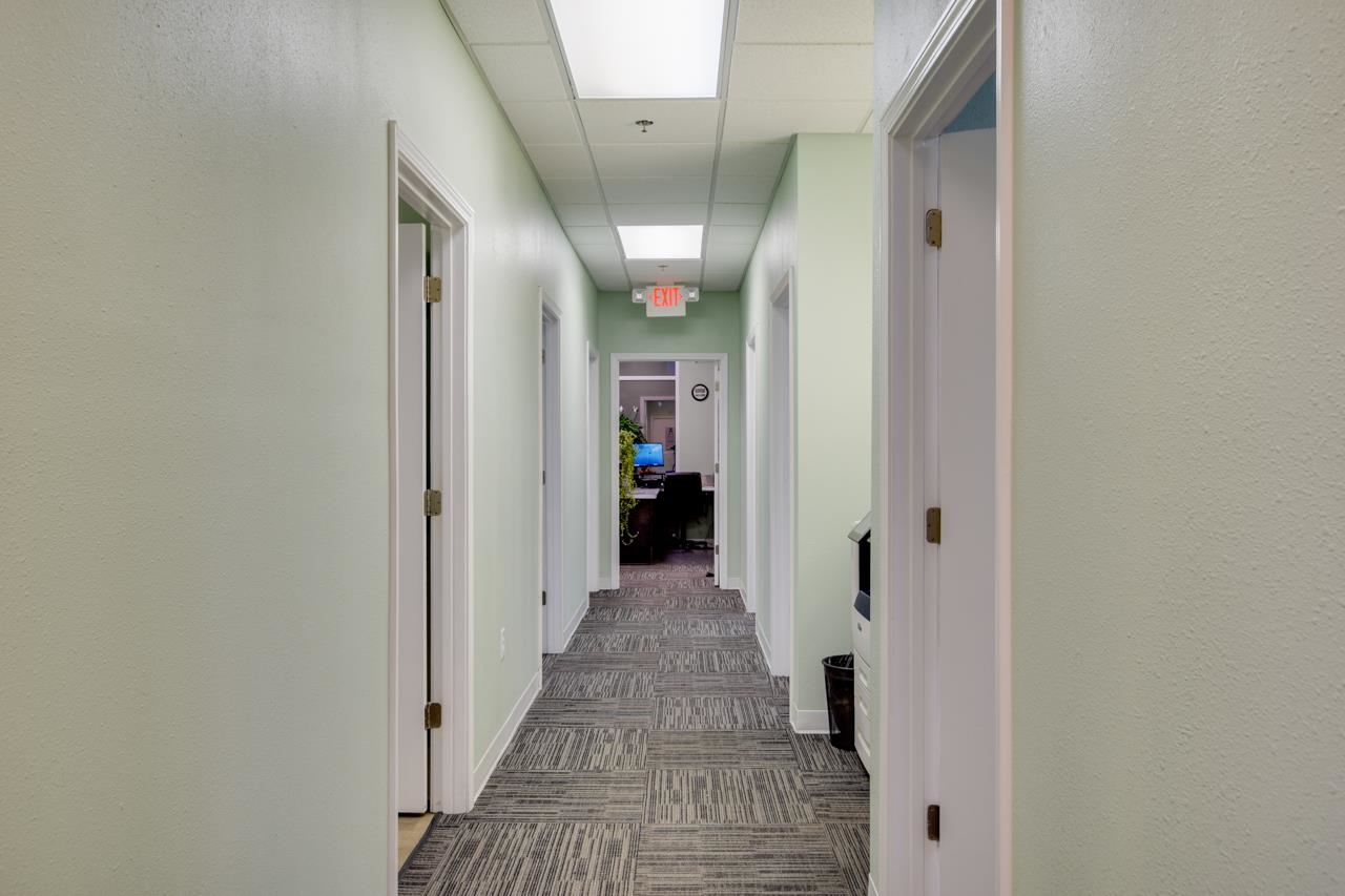 Office hallway with patterned carpet, multiple doorways, and an EXIT sign at the far end.