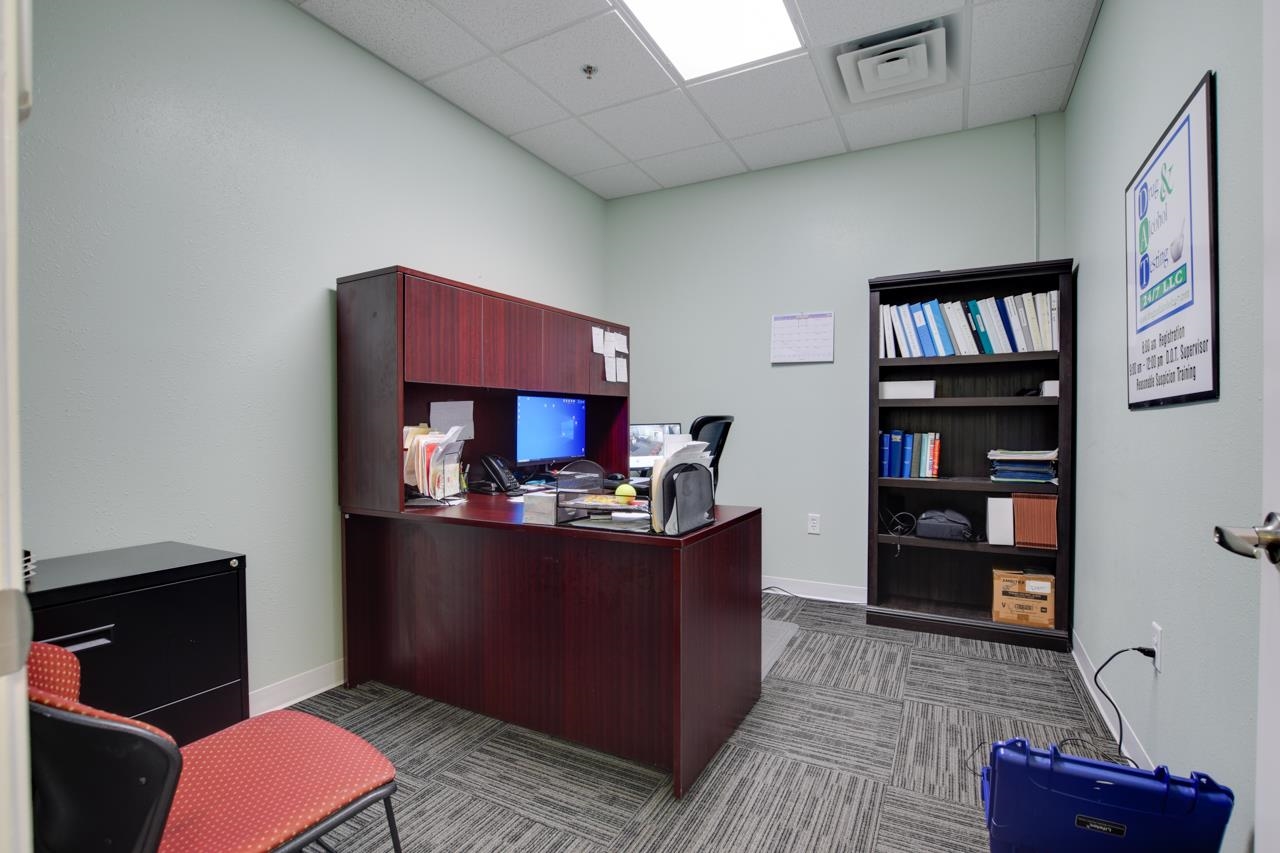 Office with a dark wood desk, filled bookcase, and red upholstered chair.