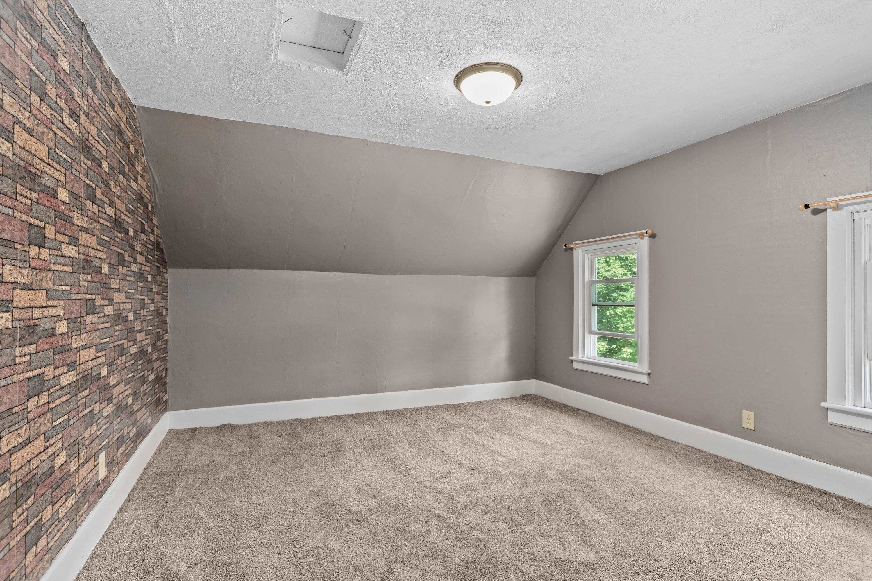 Empty bedroom with a sloped ceiling, brick-pattern accent wall, and carpet.