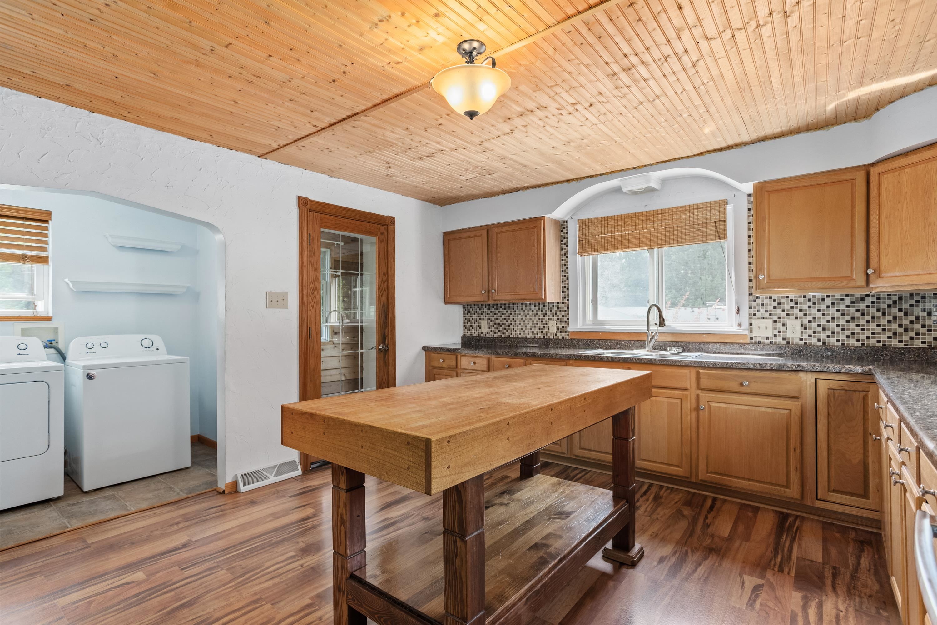 Kitchen with a large butcher-block island, wood cabinetry, and an adjoining laundry area.