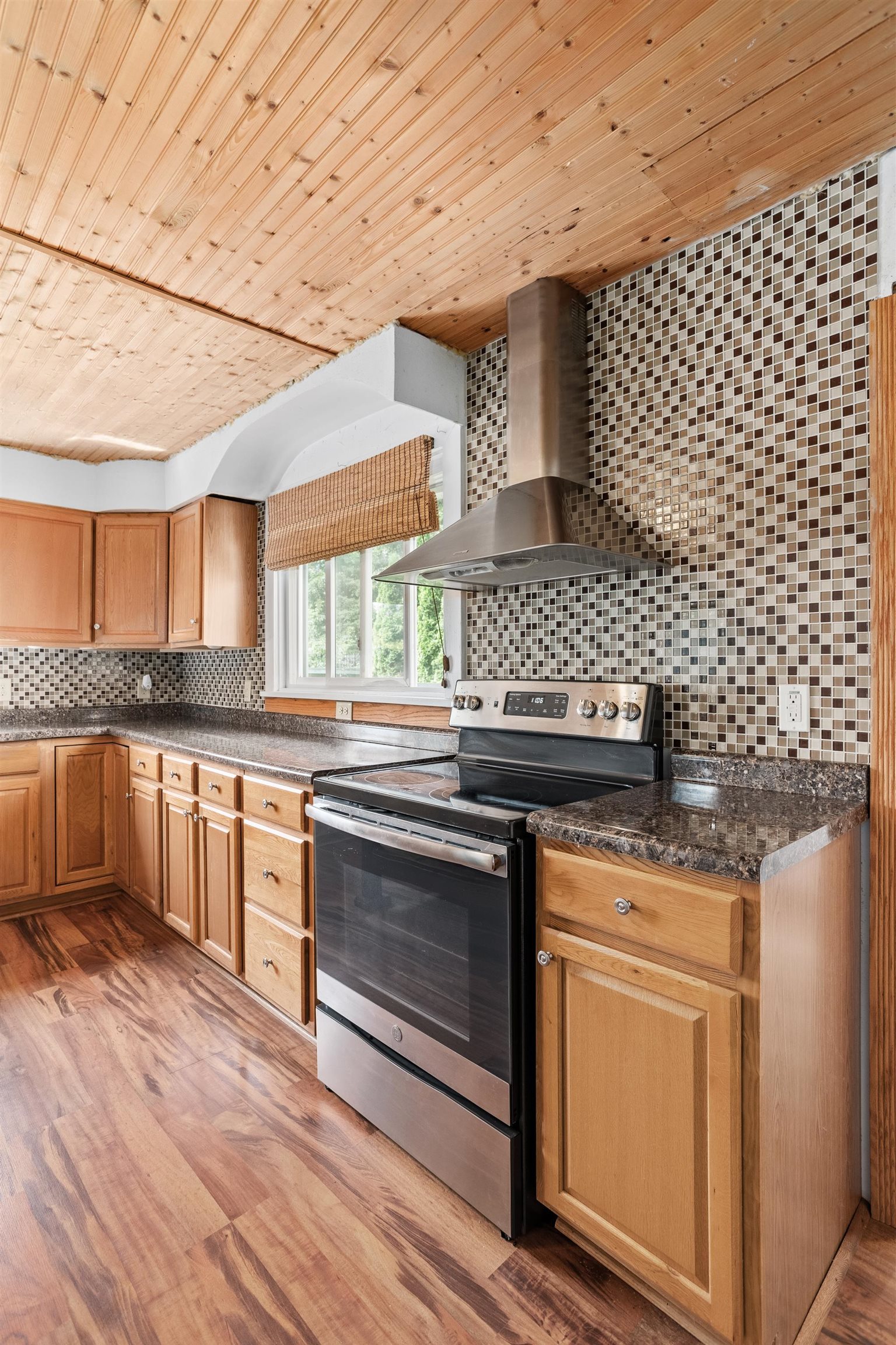 Kitchen with wood cabinets, dark countertops, tiled backsplash, and a stainless steel range beneath a wood-paneled ceiling.