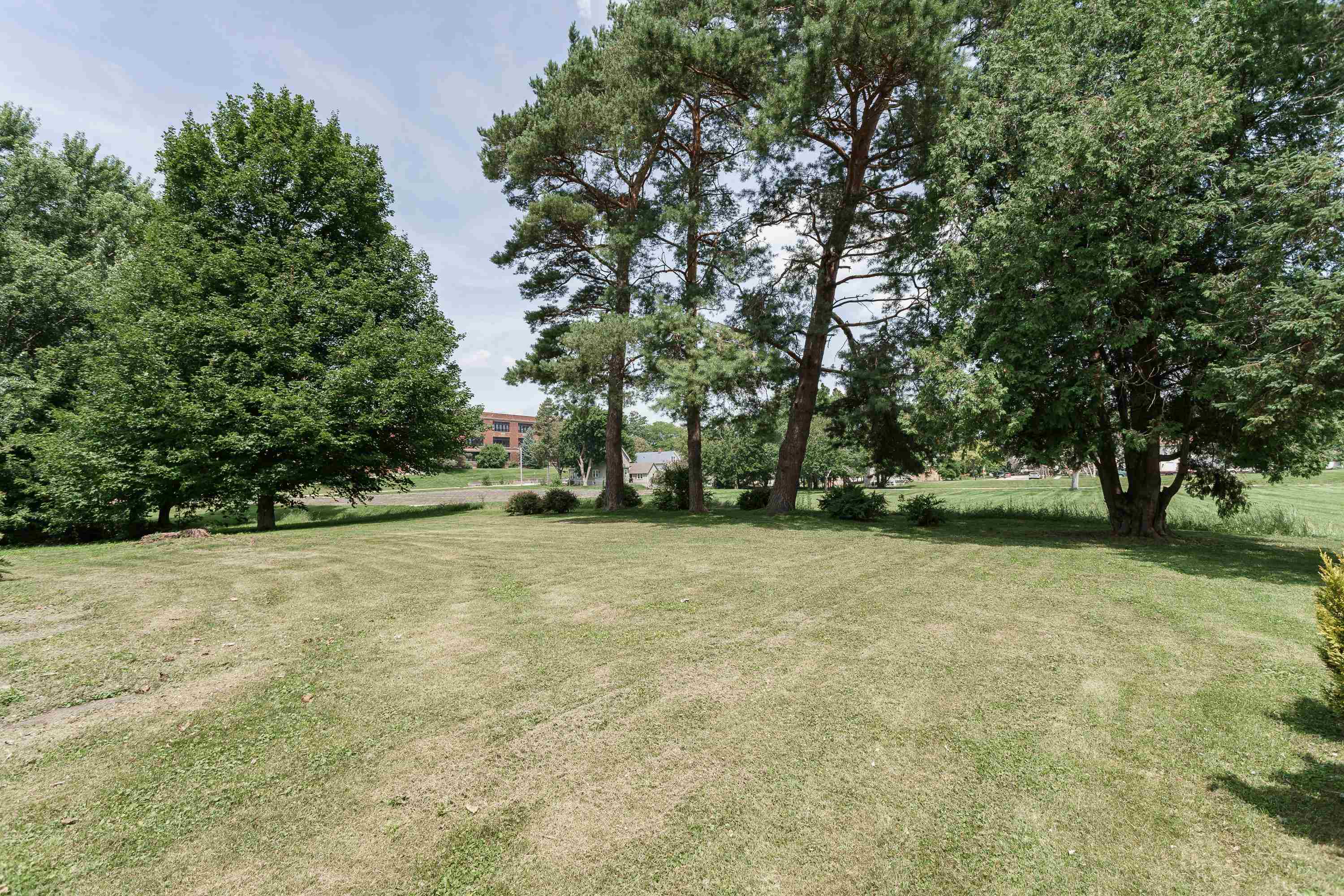 Spacious grassy yard shaded by mature trees, with buildings in the distance.