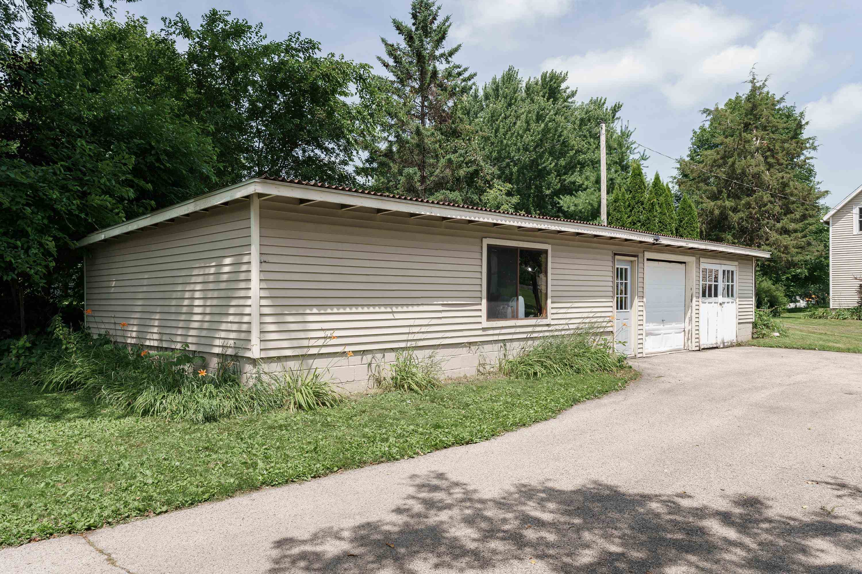 Detached light-sided garage with two garage doors, a broad roof, and a paved driveway.
