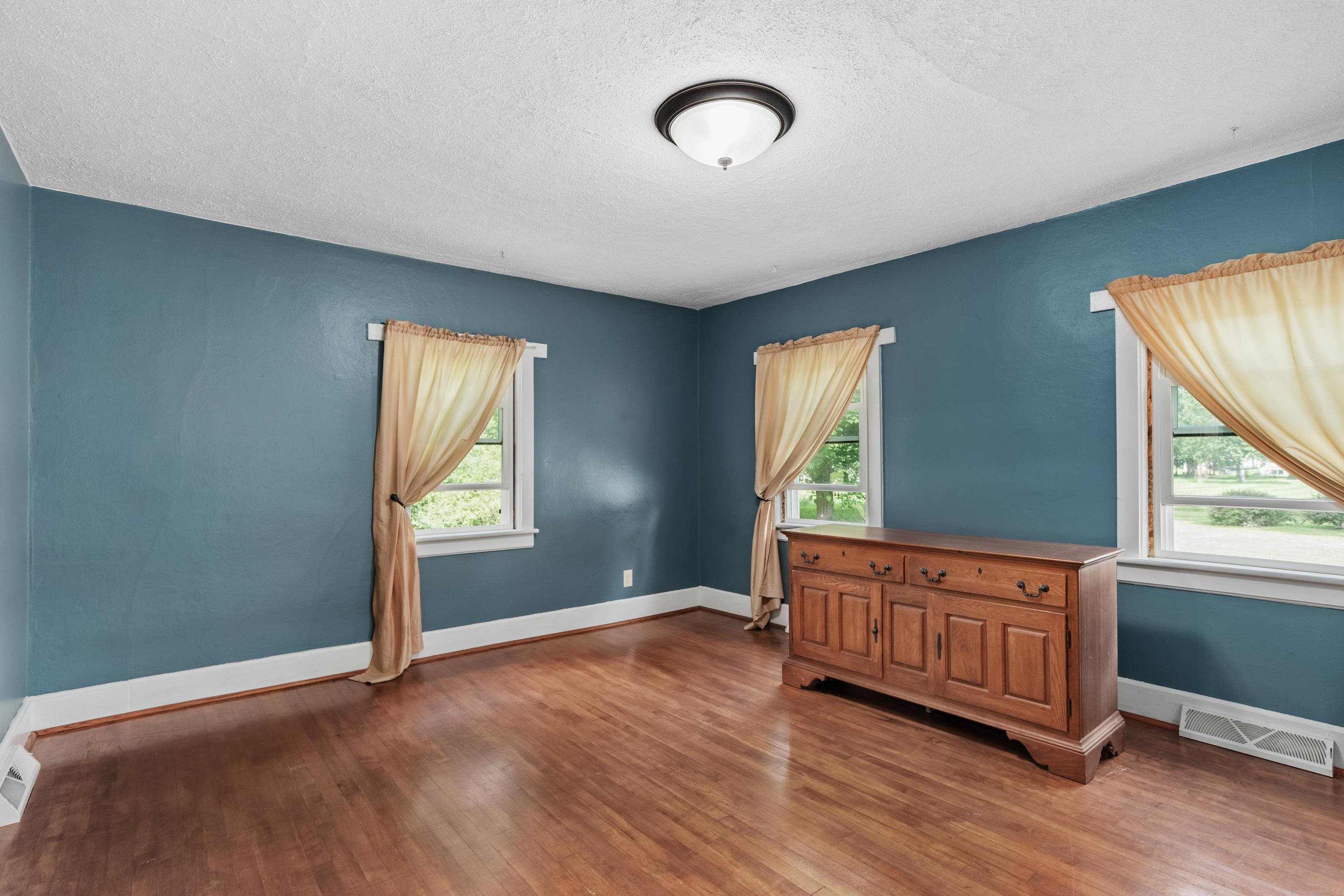 Room with blue walls, hardwood floors, three curtained windows, and a wooden dresser.