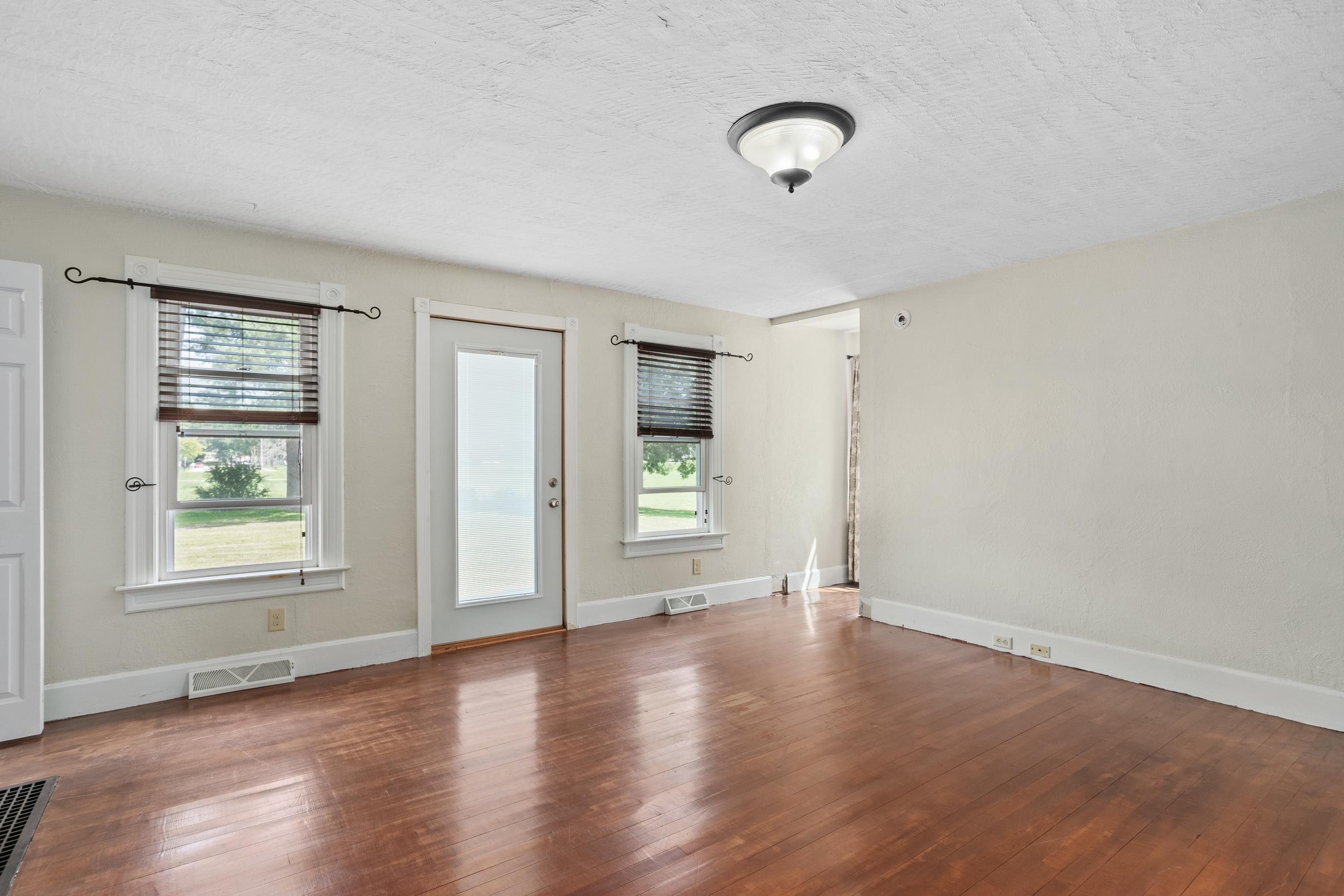 Vacant room with polished hardwood floors, two windows, and a glazed exterior door.
