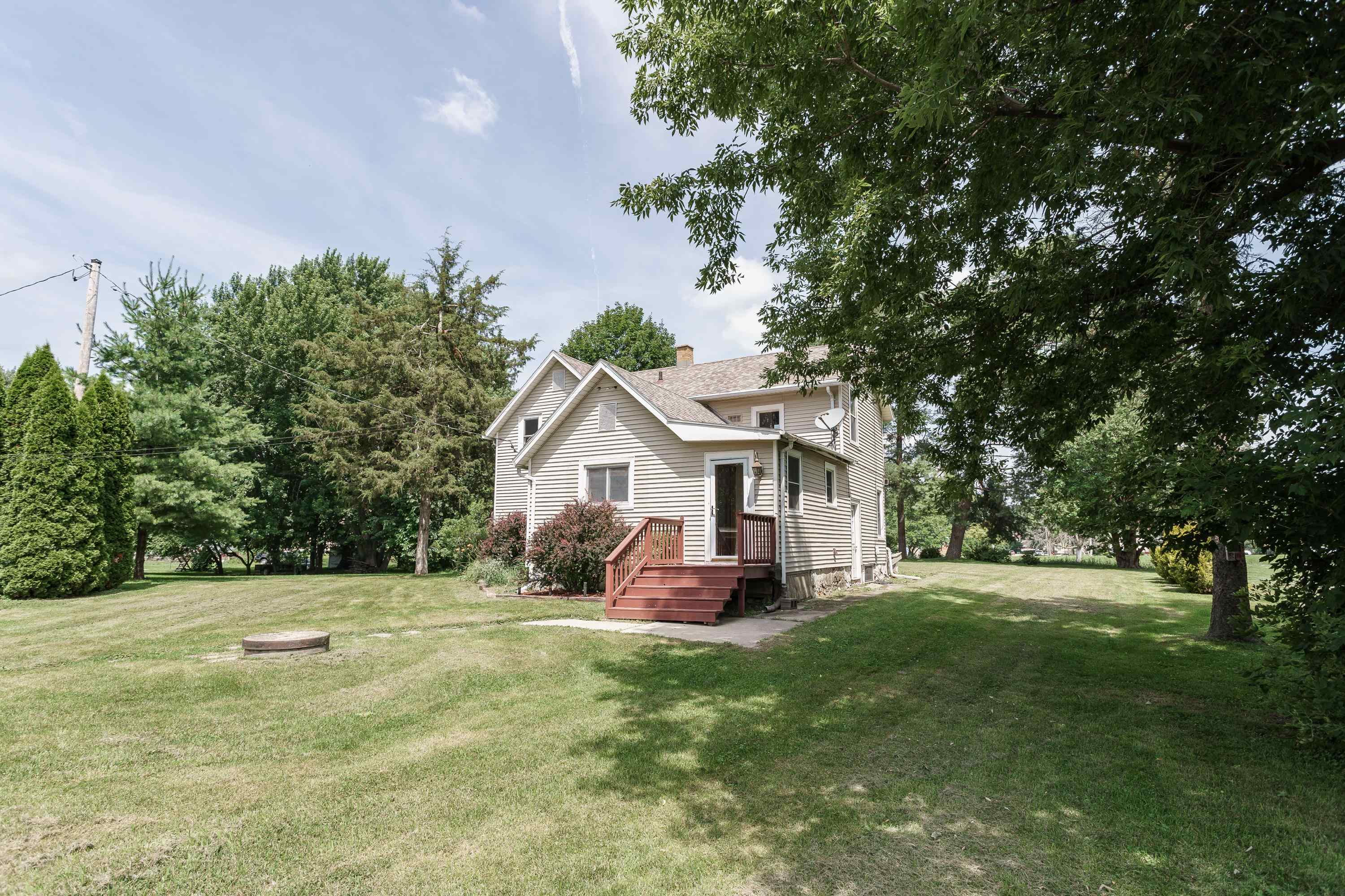 Two-story light-sided house with red steps, surrounded by mature trees and a broad lawn.