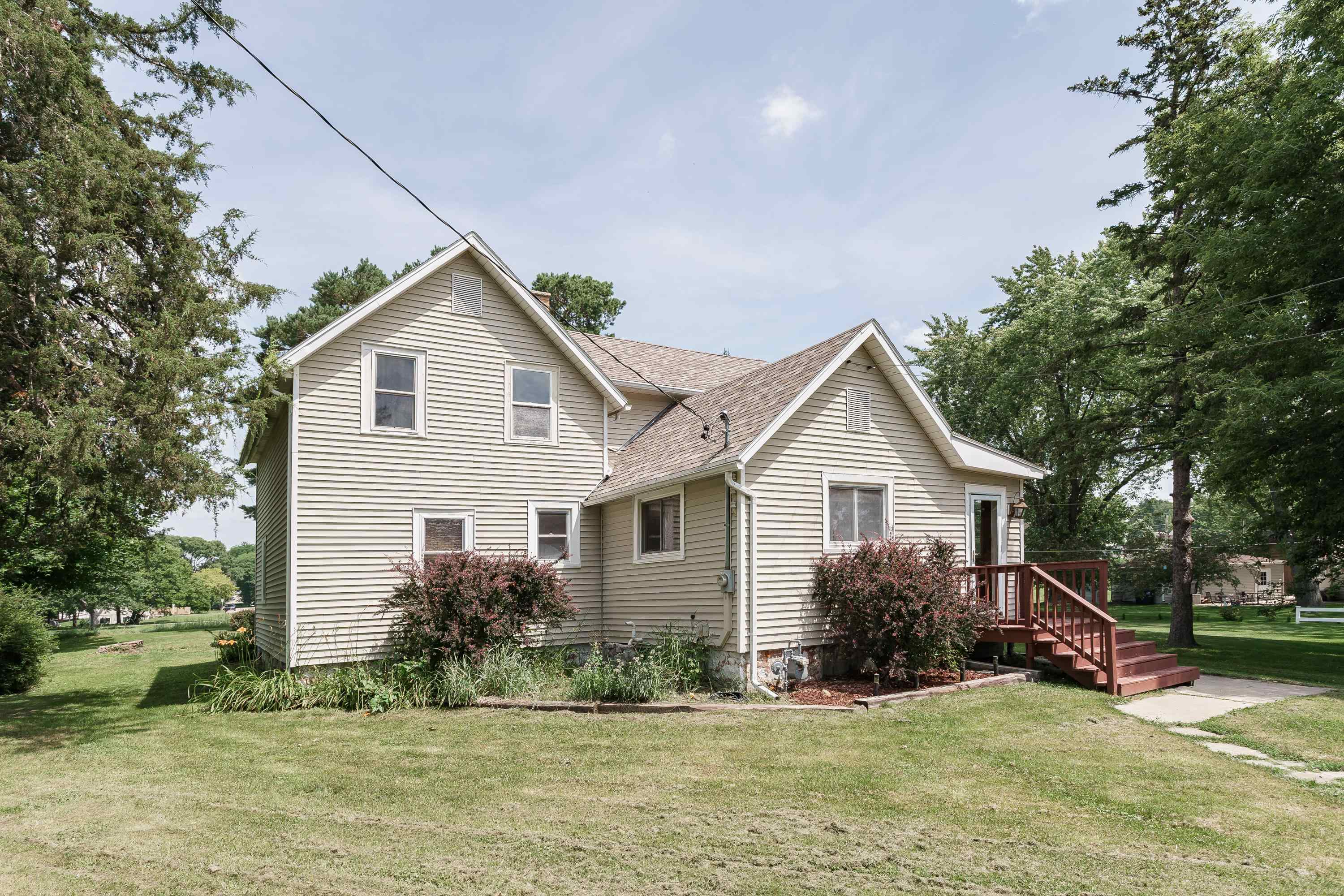Beige-sided home with multiple gables, red entry stairs, and a broad lawn.