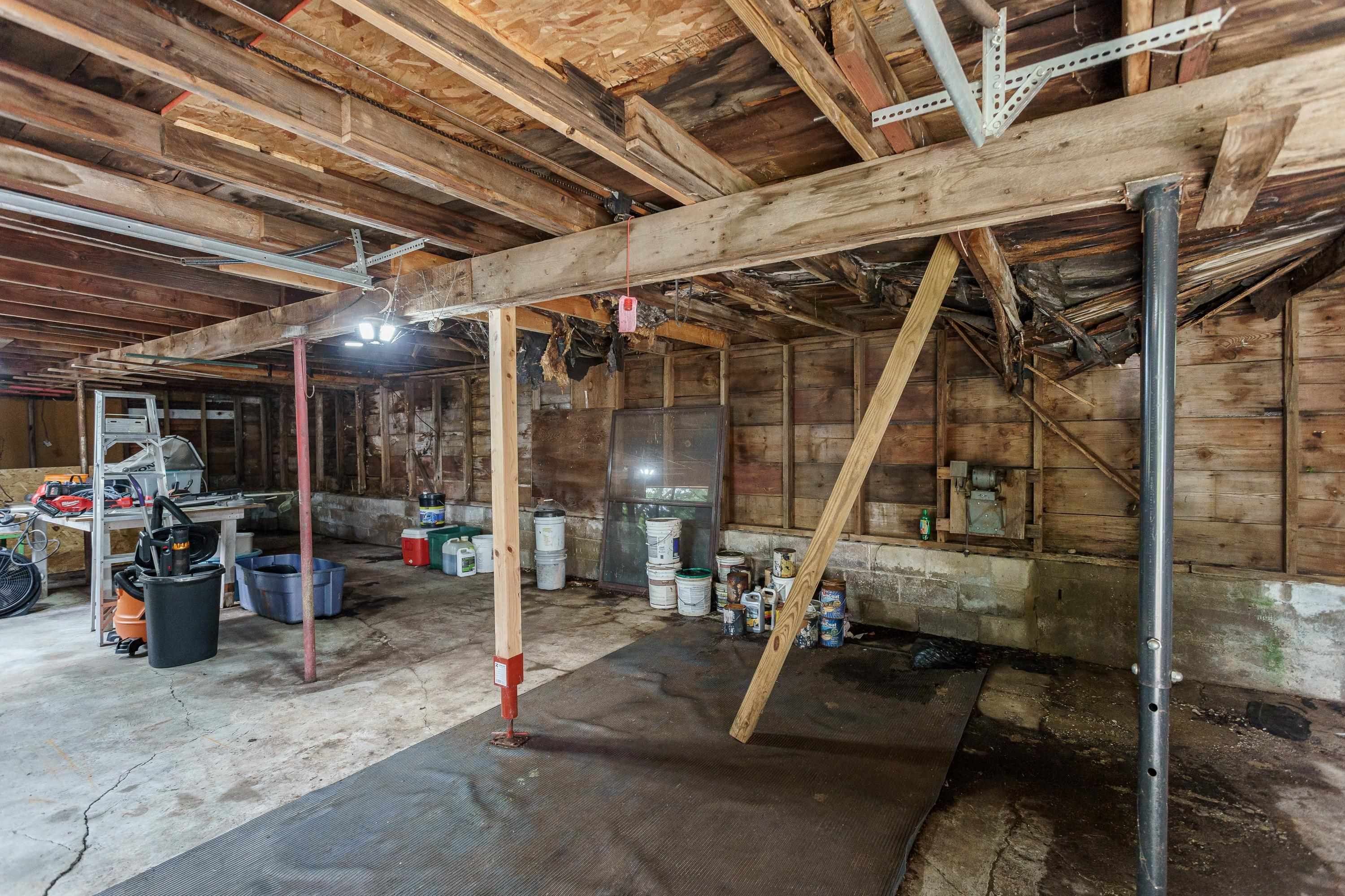 Unfinished basement with exposed framing, support posts, and tools and supplies stored along the walls.