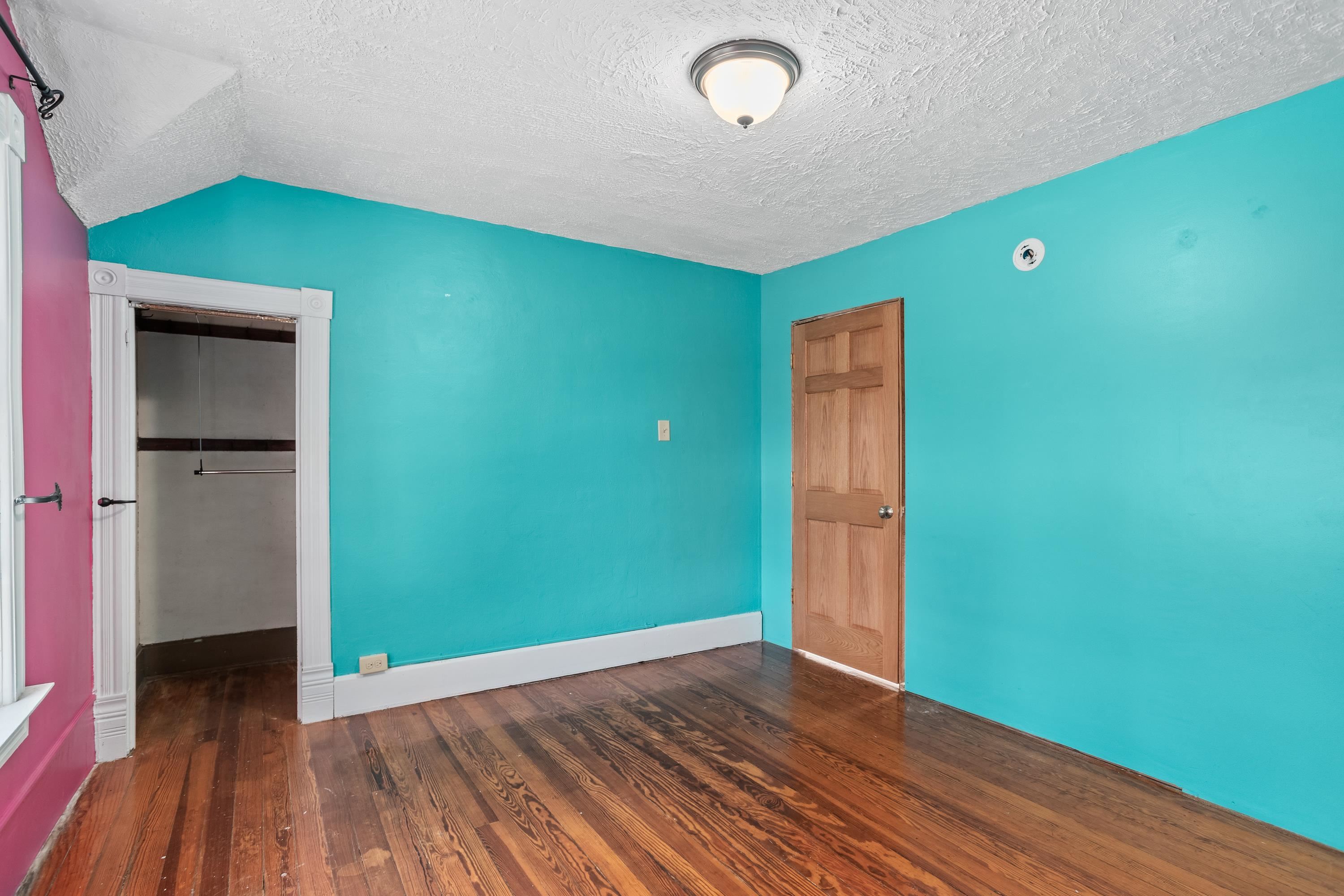 Empty bedroom with turquoise walls, a pink accent wall, hardwood floors, and an open closet.