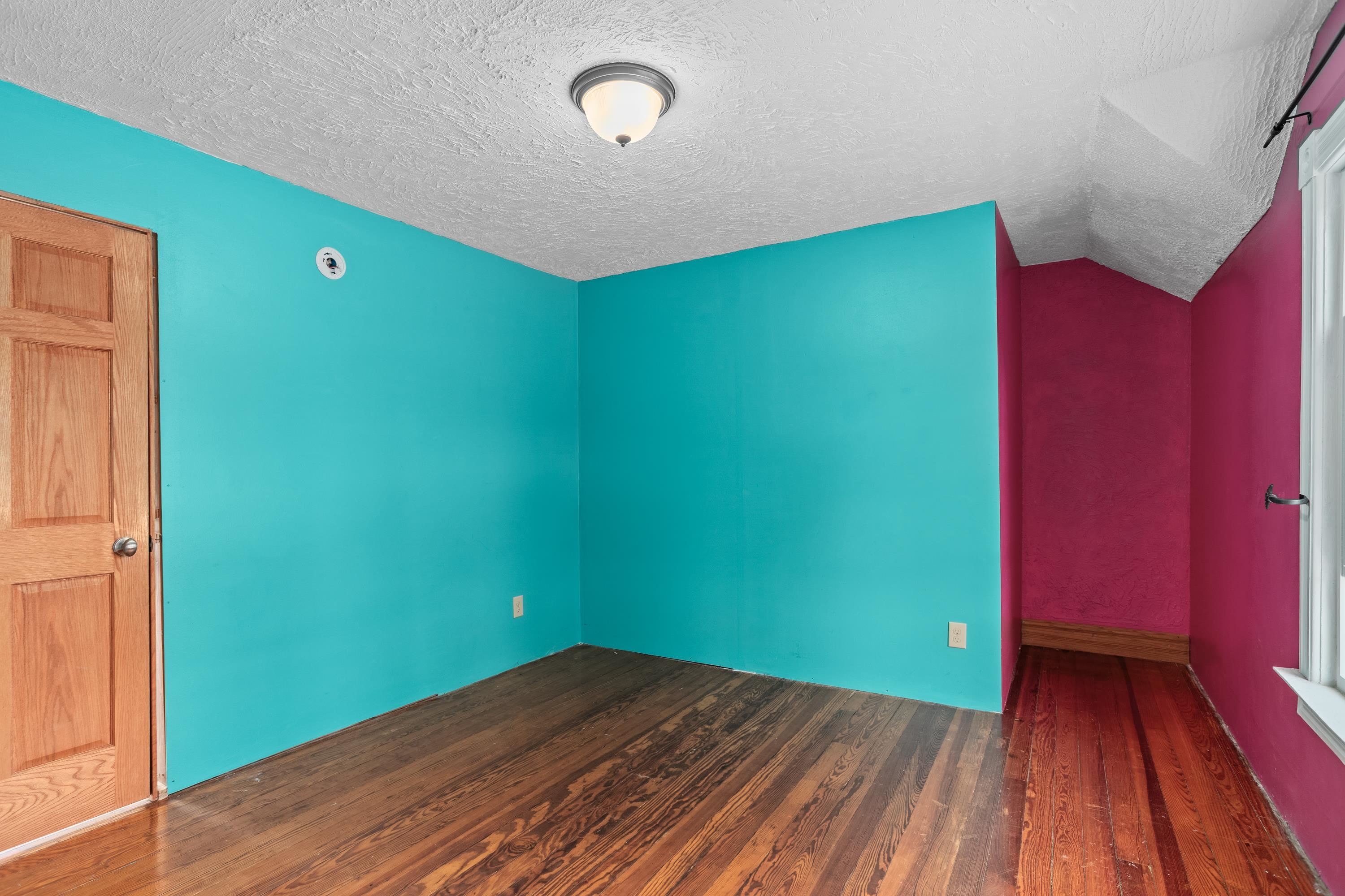 Unfurnished room with vivid turquoise and magenta walls, dark wood floors, and a sloped ceiling.