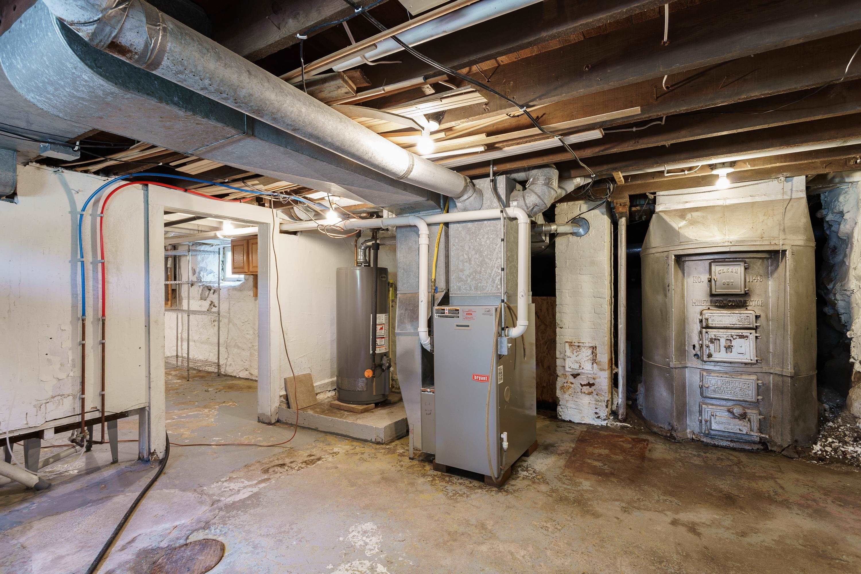 Basement mechanical room with a Bryant furnace, water heater, and large older metal heating unit.