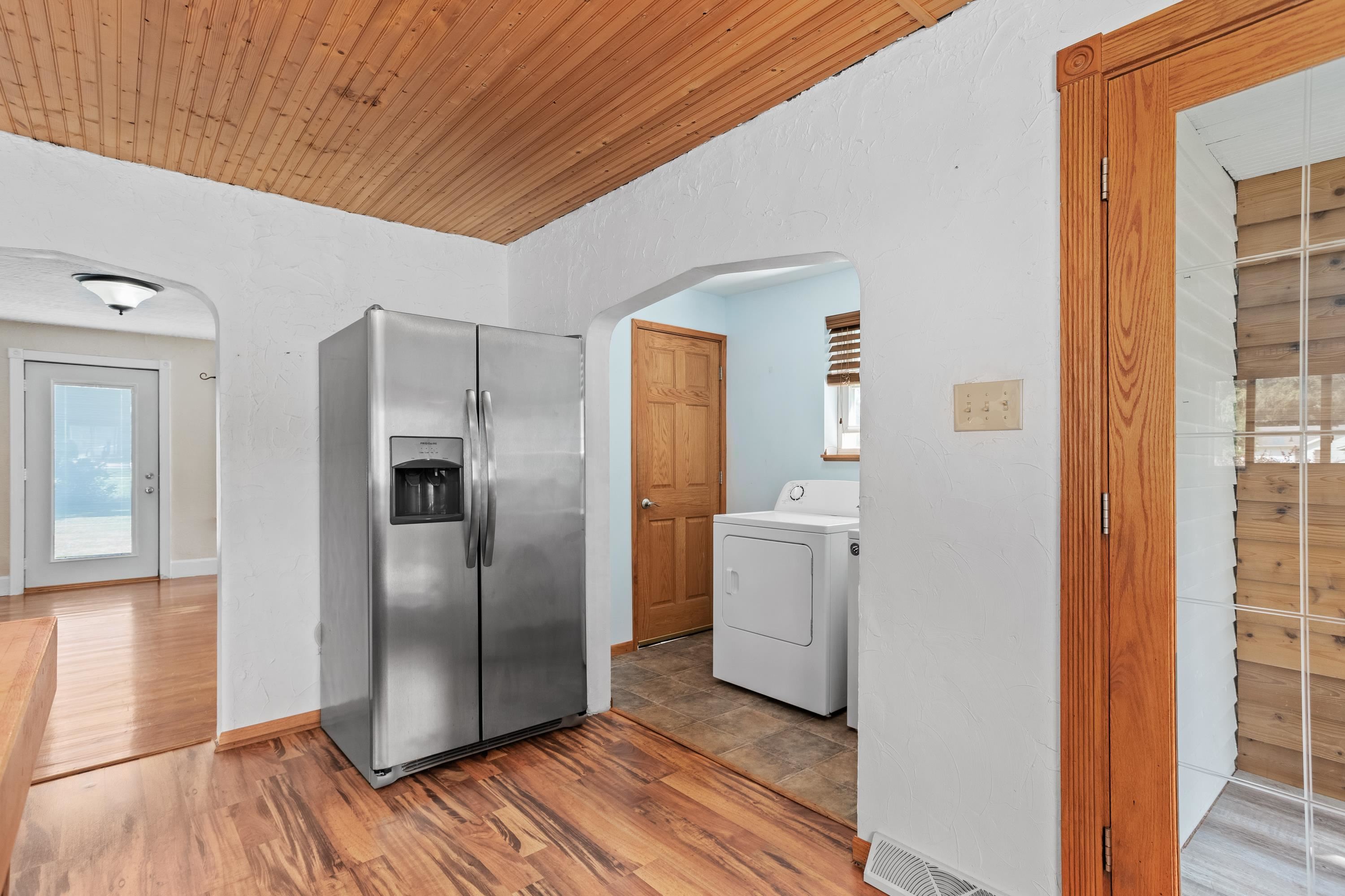 Interior with a stainless steel refrigerator beside a laundry alcove and white dryer.