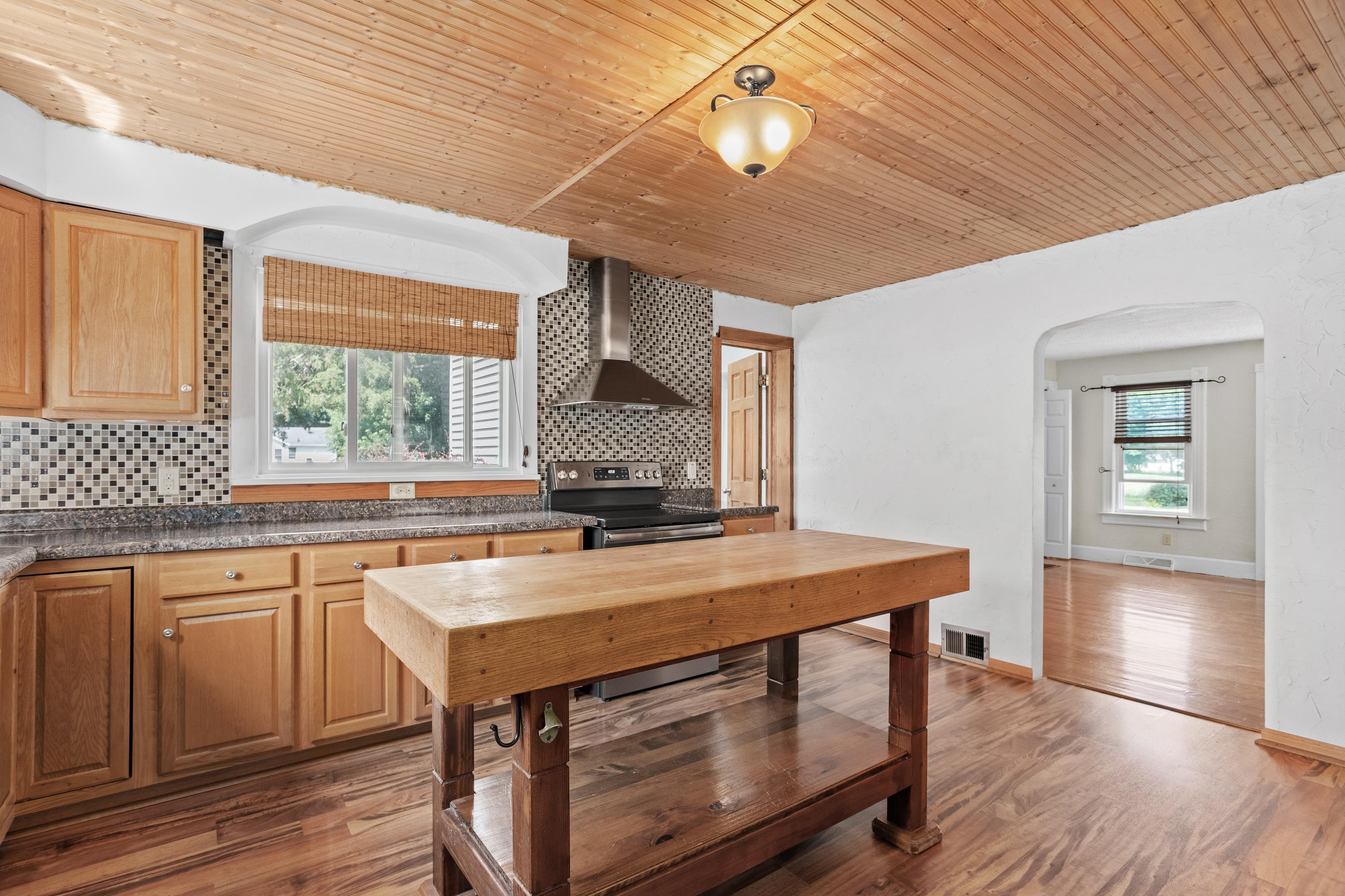 Kitchen with a large wooden island, mosaic tile backsplash, and wood-plank ceiling.