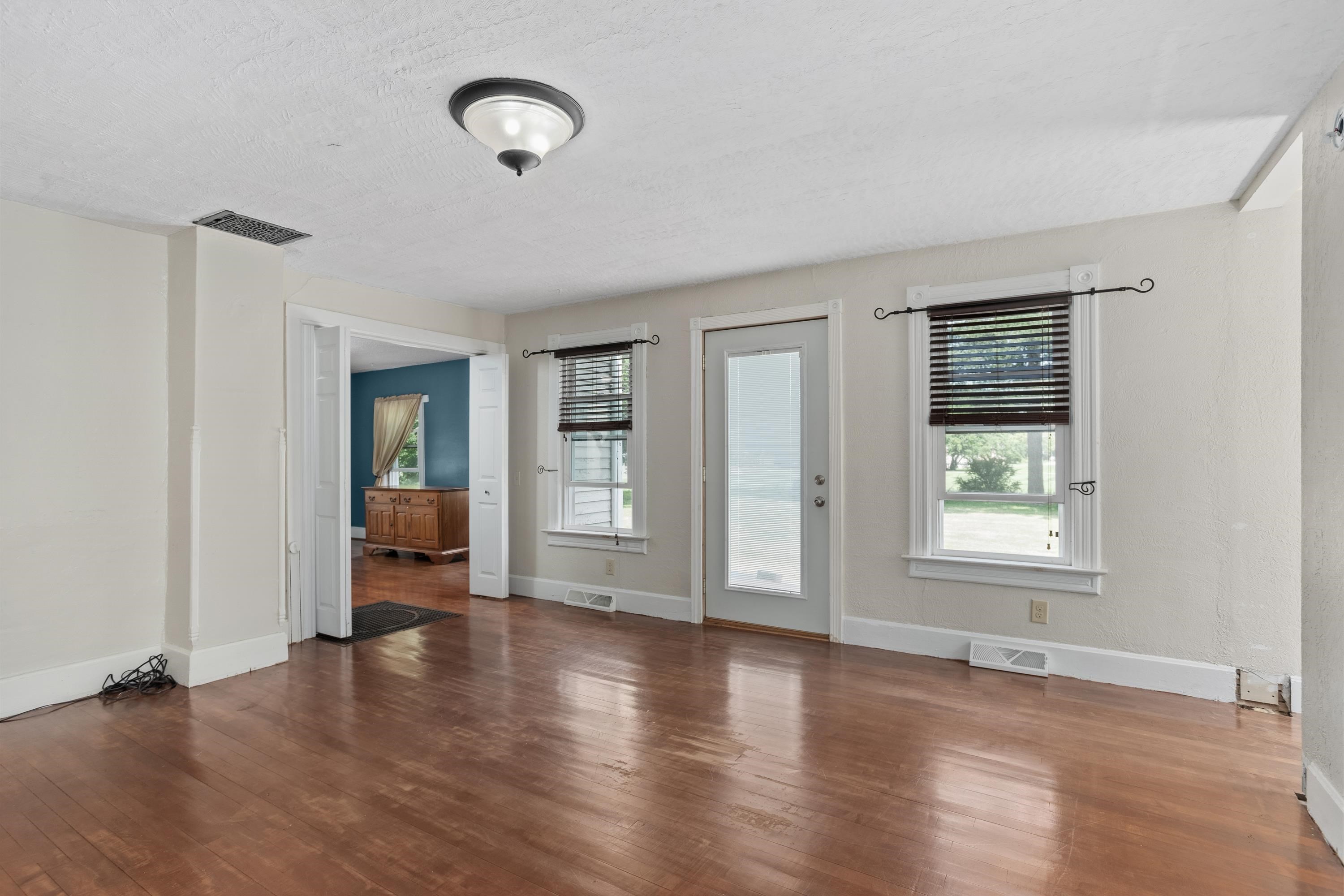 Empty room with worn hardwood floors, two blind-covered windows, and a glass-paneled exterior door.