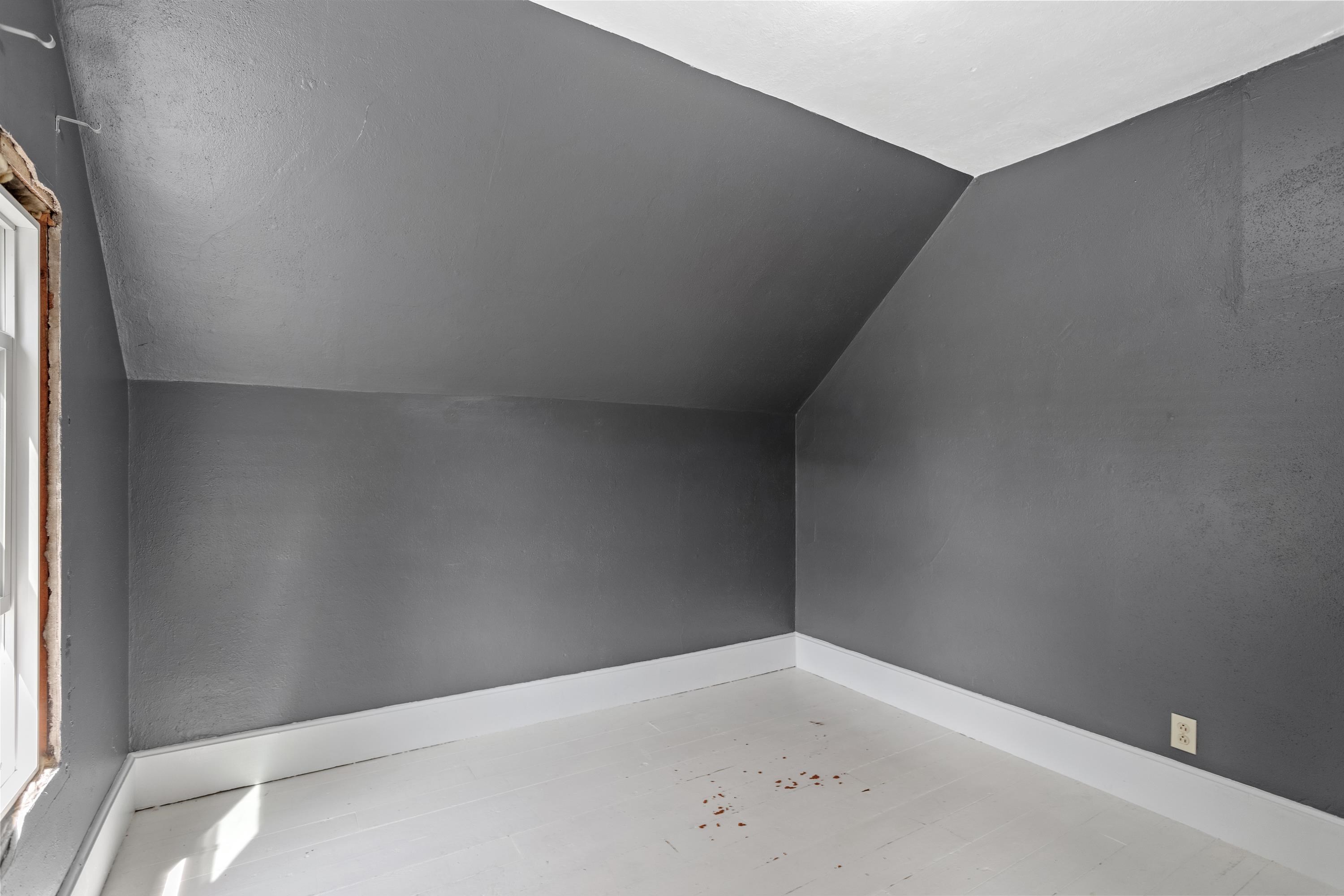 Empty room with dark gray walls, sloped ceiling, white plank floor, and a window.