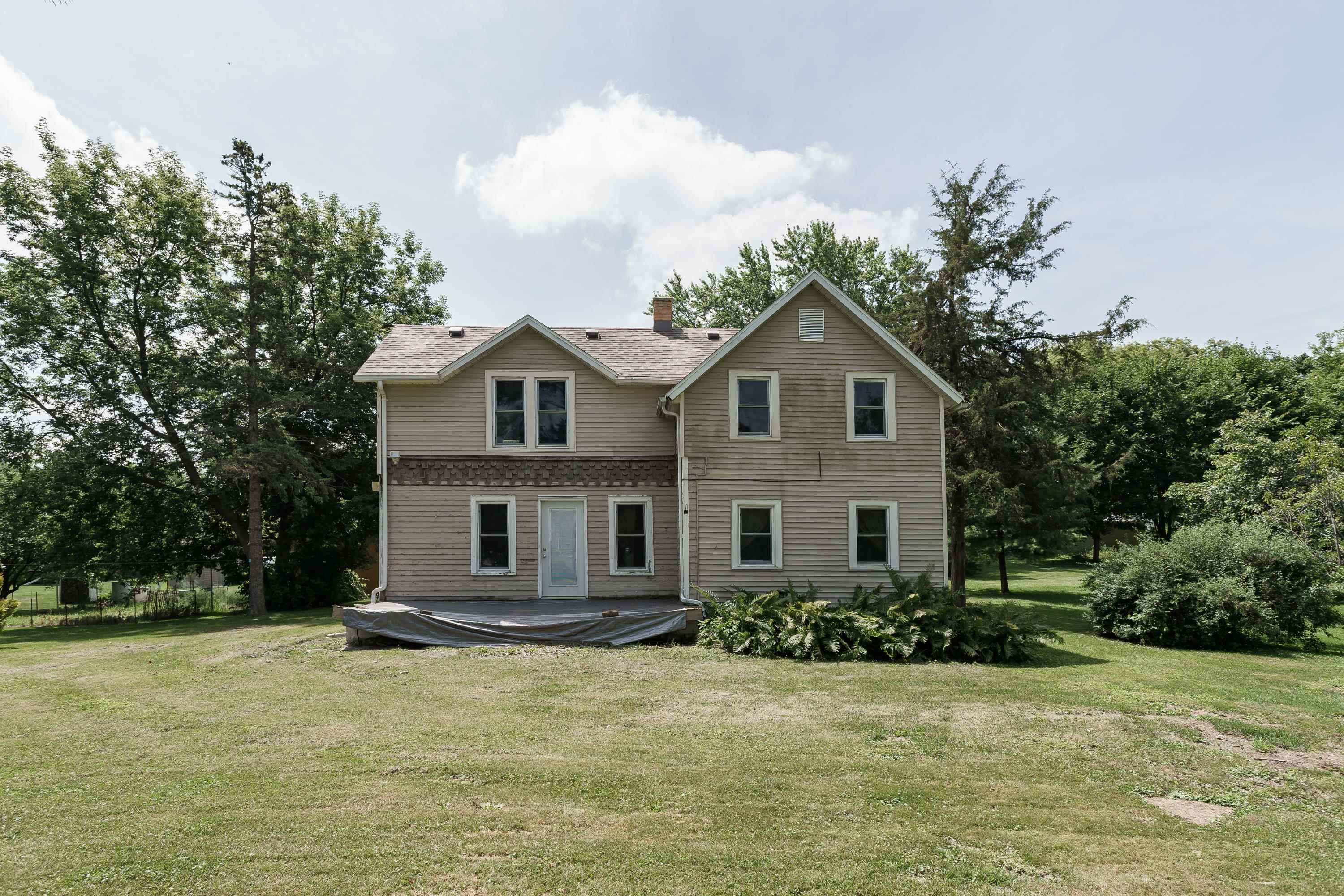 Rear of a two-story beige house with multiple gables, a raised deck, and a tree-lined lawn.