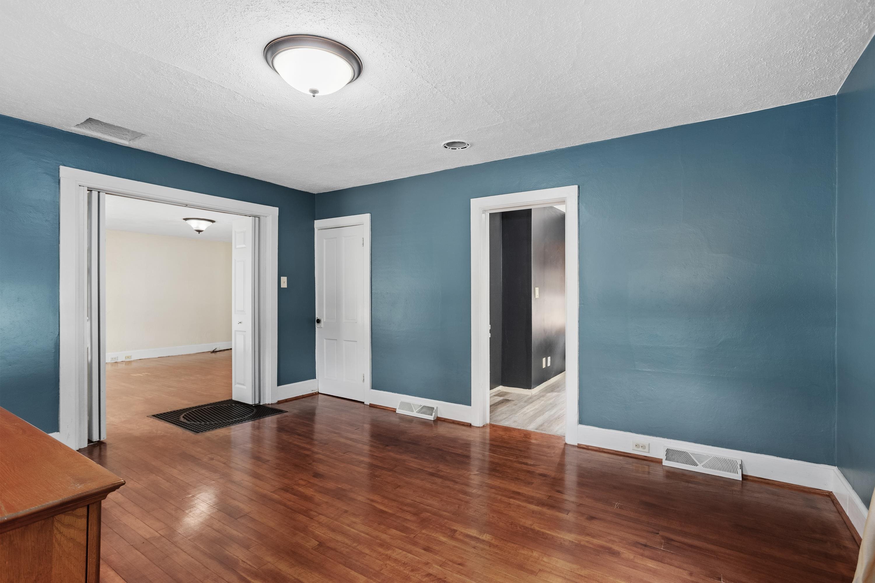 Empty blue-walled room with polished hardwood floors and doorways to adjoining rooms.