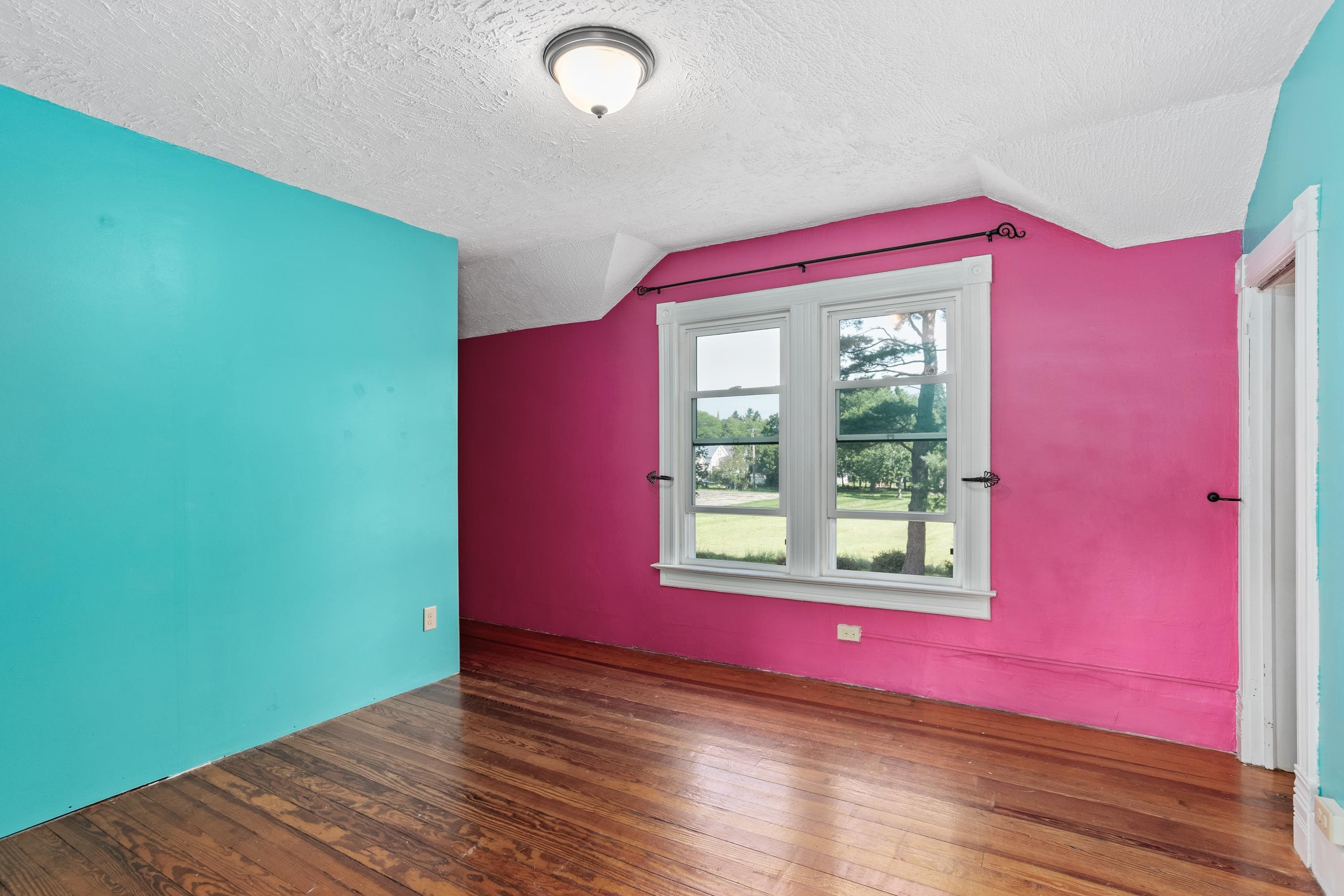 Empty bedroom with turquoise and pink walls, hardwood floors, and a double window.