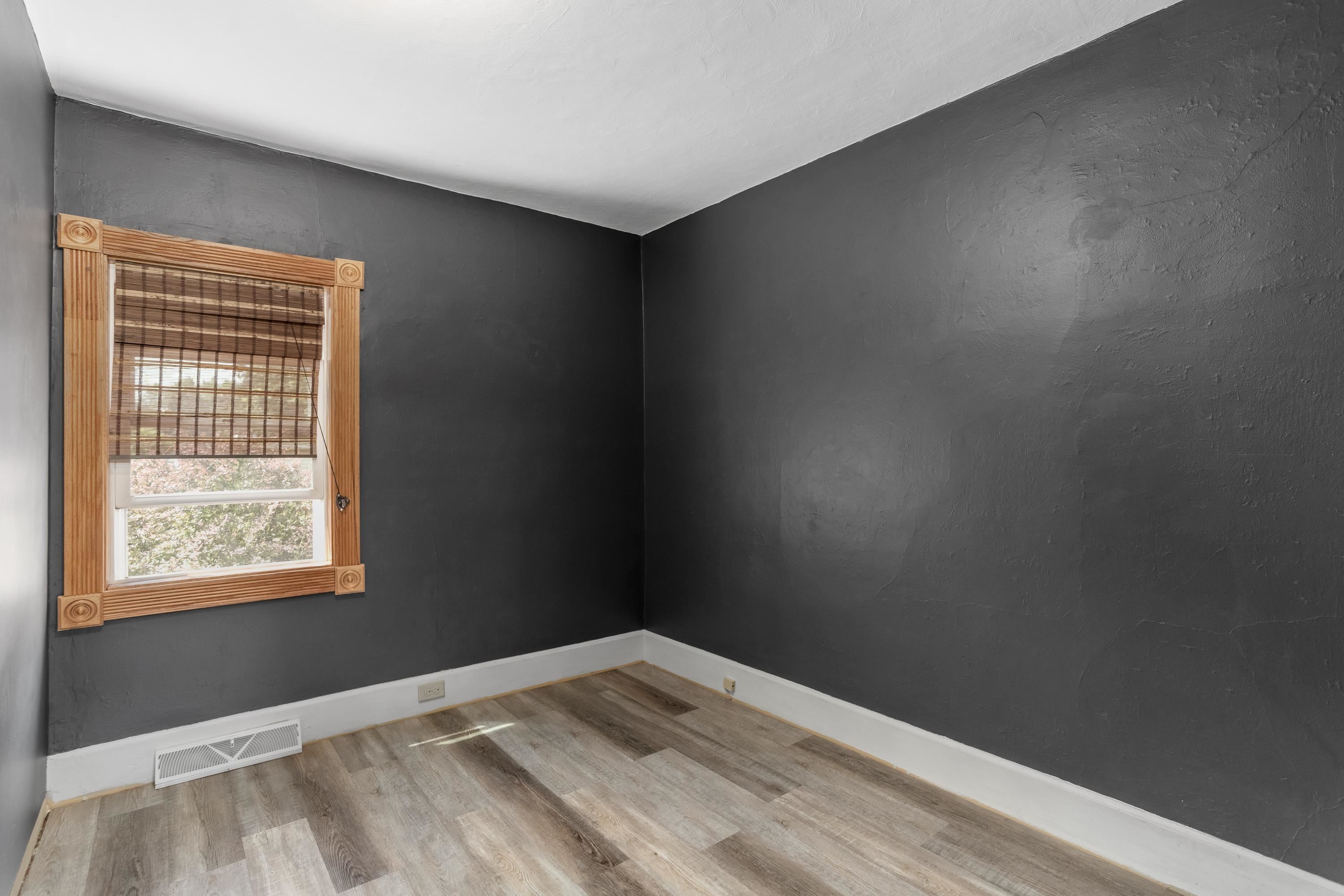 Empty room with charcoal walls, gray wood-look flooring, and a wood-trimmed window with a woven shade.