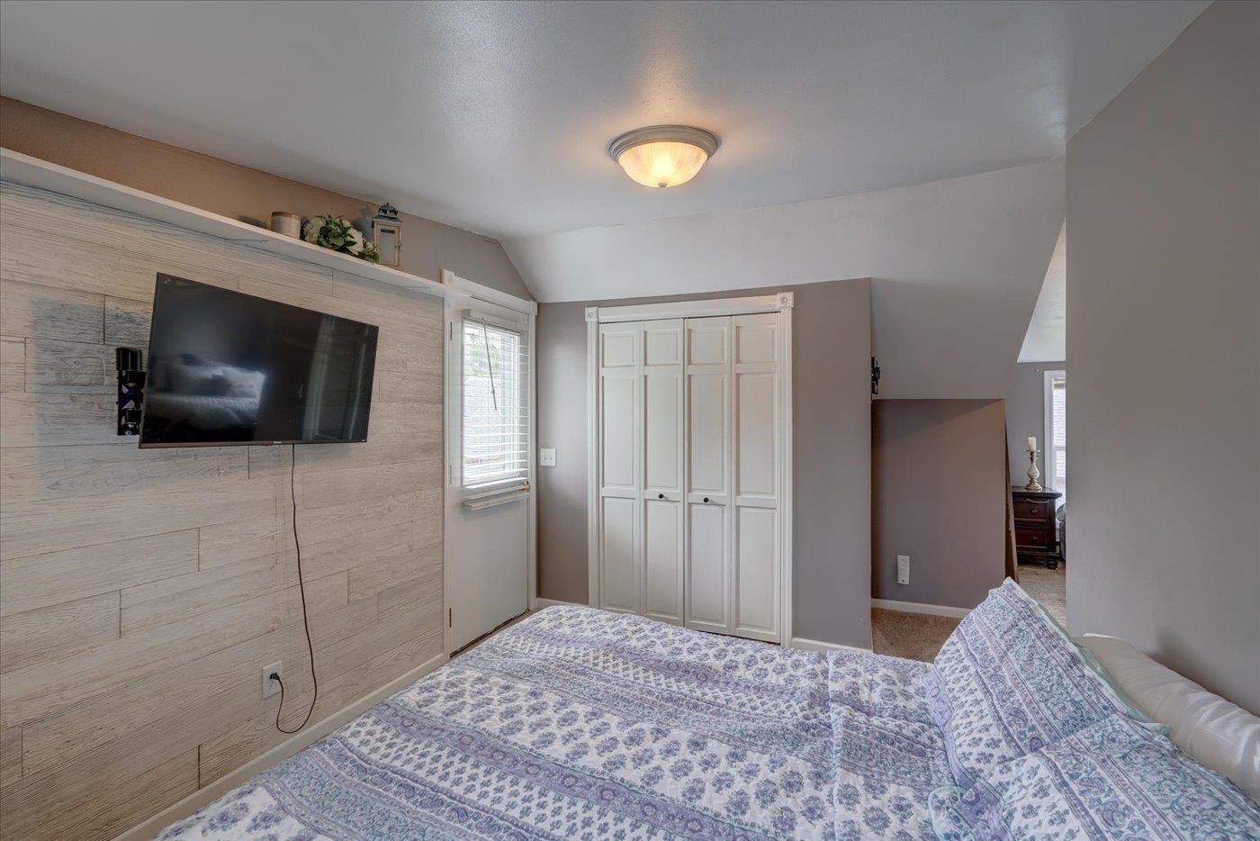 Bedroom with a patterned bedspread, wall-mounted TV, and white closet doors.