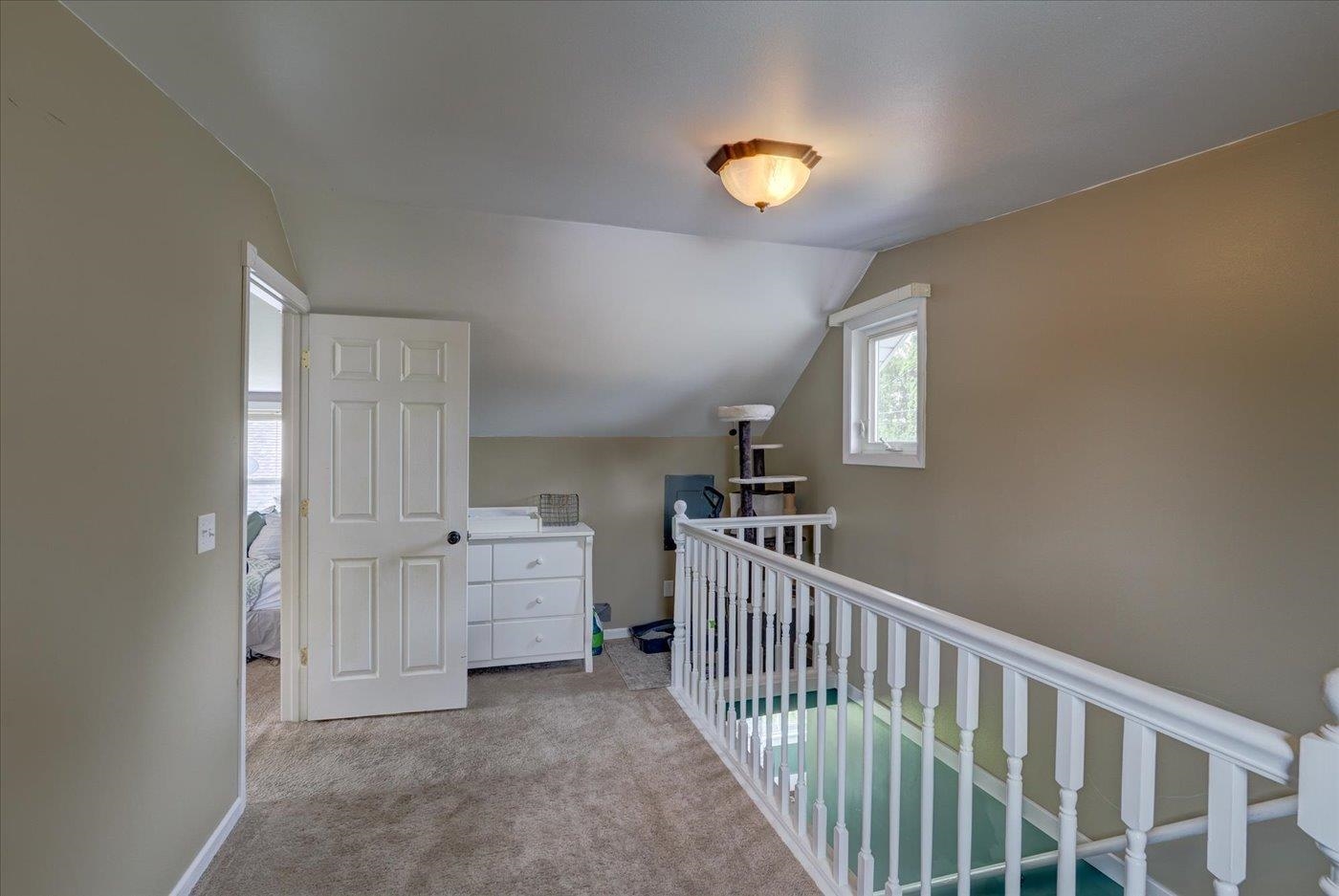 Carpeted upstairs landing with a white railing, sloped ceiling, and small window.